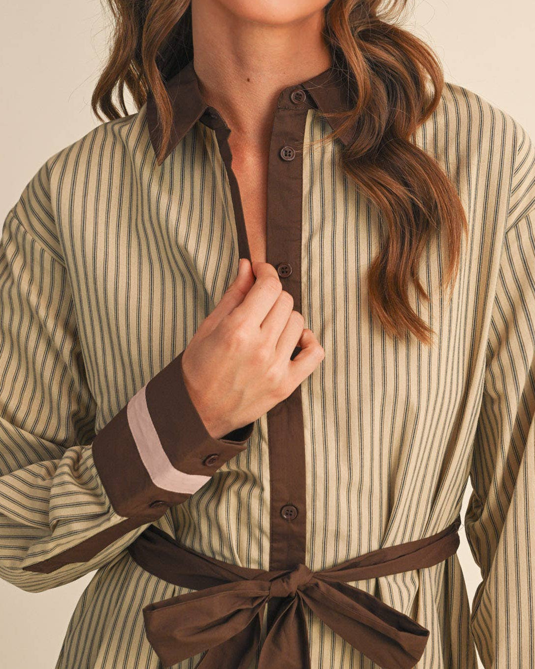 Model wearing a beige and brown striped belted mini dress on a neutral background.