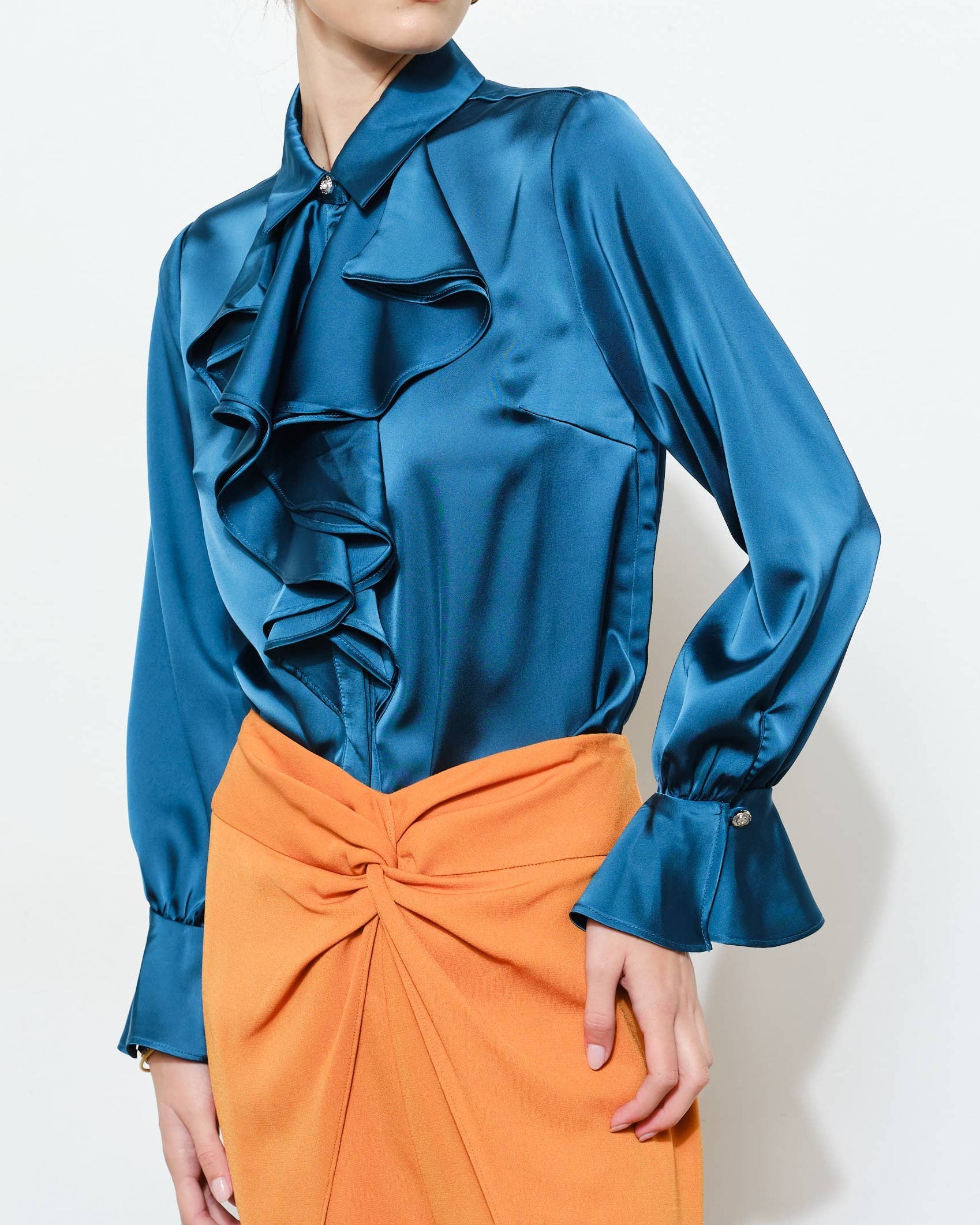 Woman wearing a blue satin blouse with ruffled details and an orange skirt on a white background