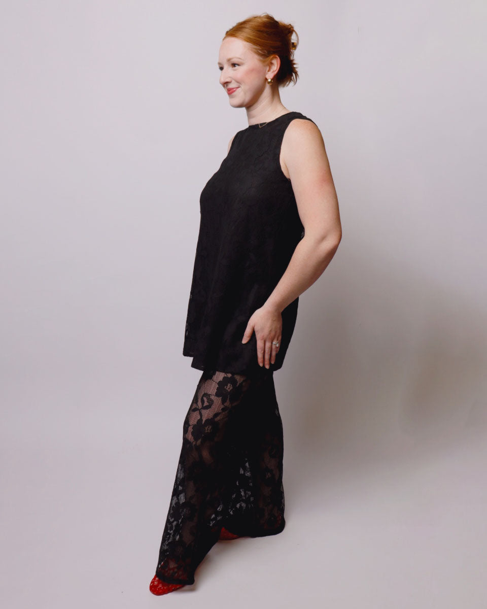 Woman wearing a black sleeveless top and black lace pants on a plain background