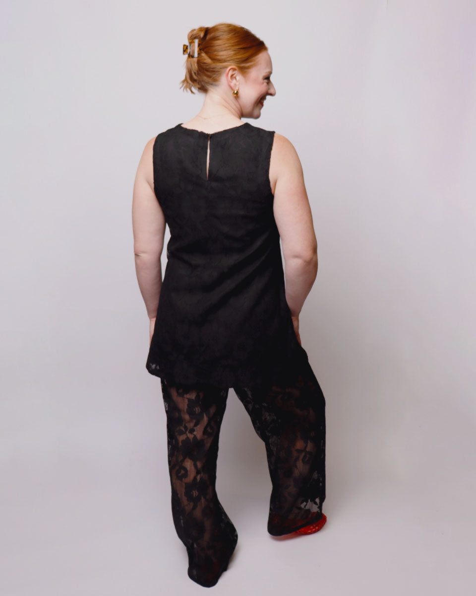 Person wearing a black sleeveless top and black lace pants on a plain background