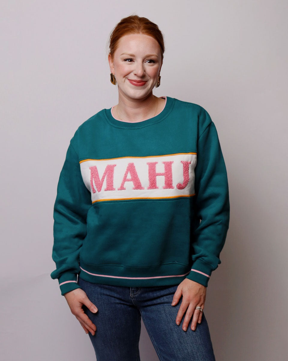 Person wearing a teal sweatshirt with 'MAHJ' printed on it against a plain background