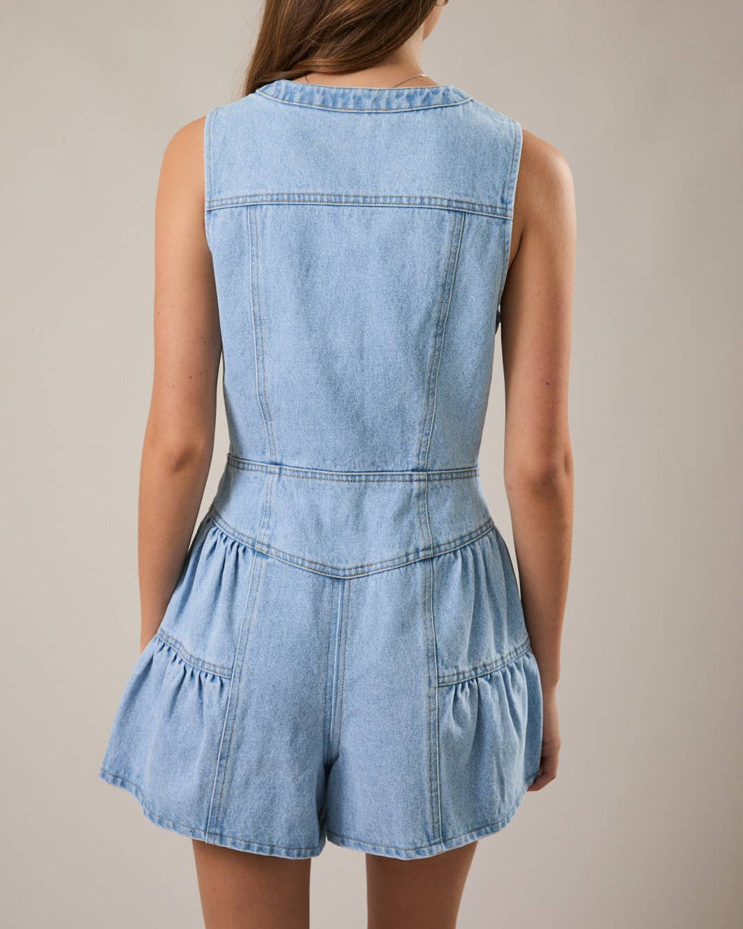 Light blue denim romper worn by a person on a beige background