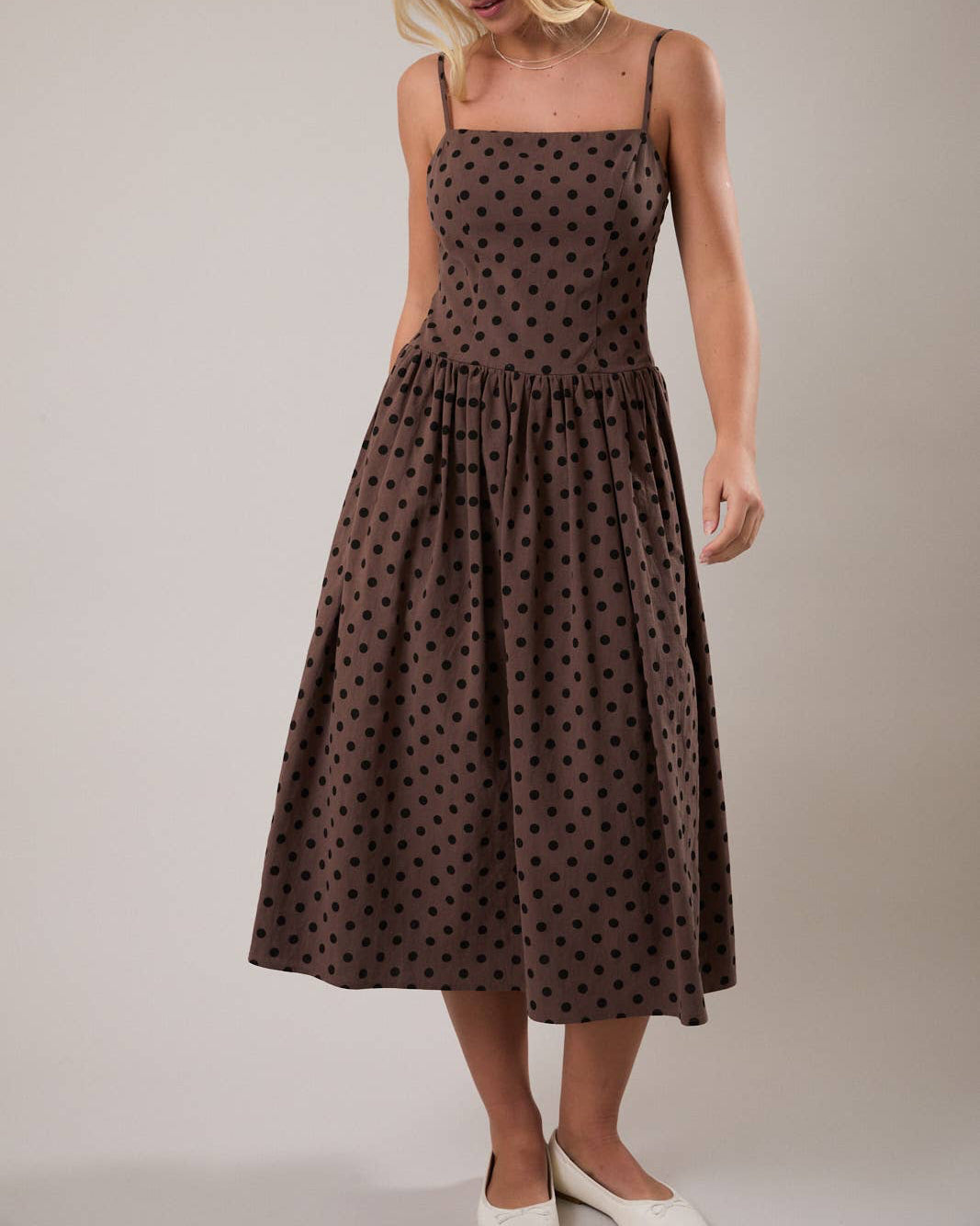 Woman wearing a brown polka dot dress against a plain background