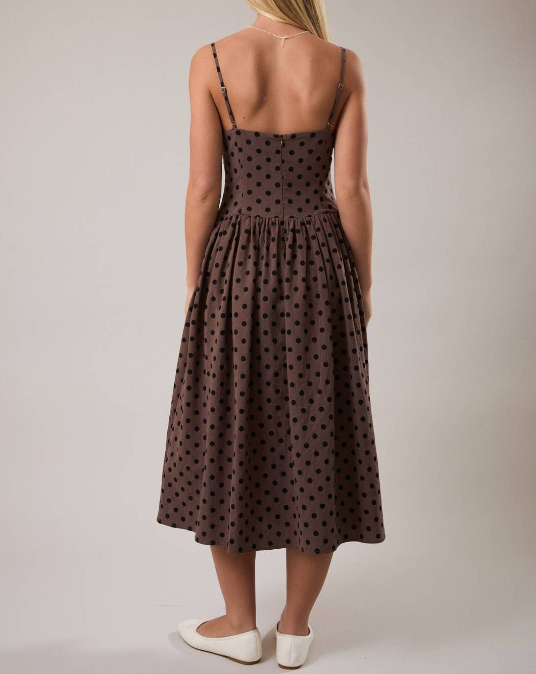 Woman wearing a brown polka dot dress against a plain background