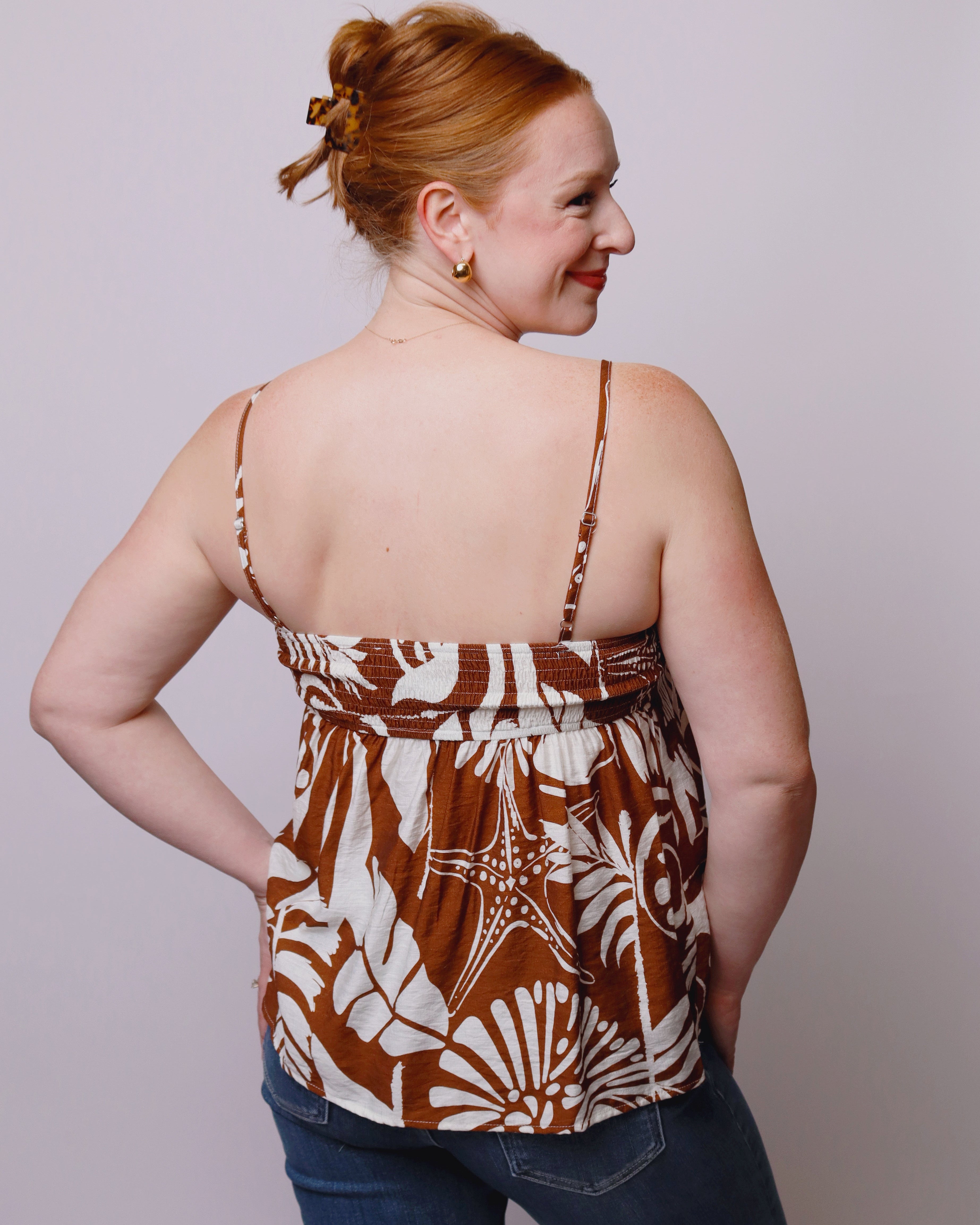 Woman wearing a brown and white patterned top with blue jeans against a plain background