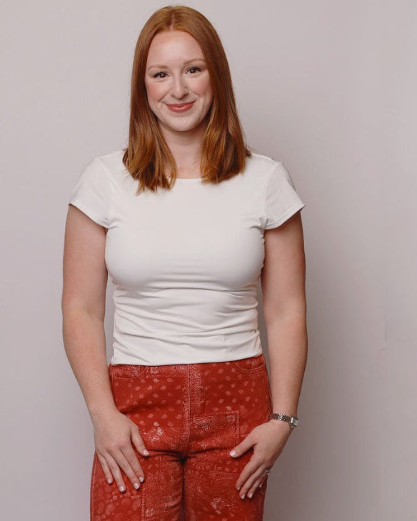Woman wearing a white top and red patterned pants against a plain background