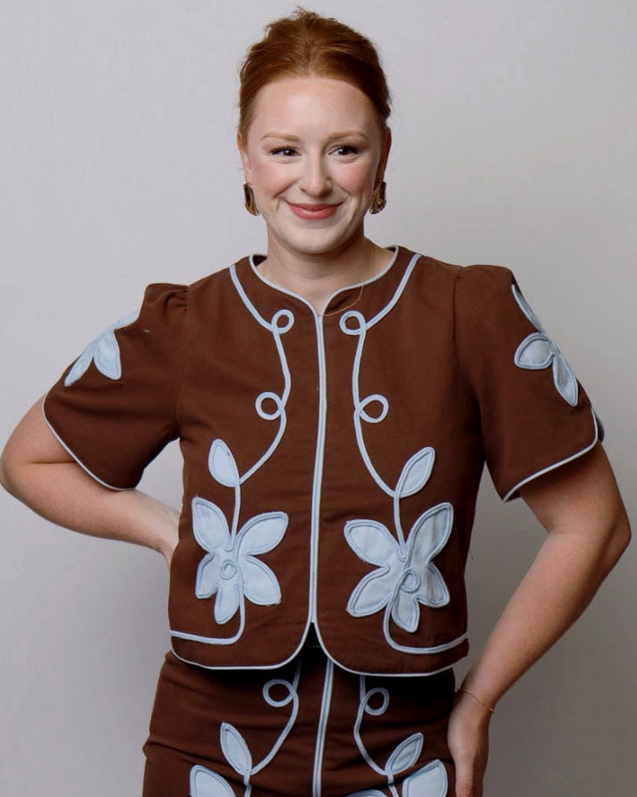 Woman wearing a brown outfit with white floral patterns on a plain background