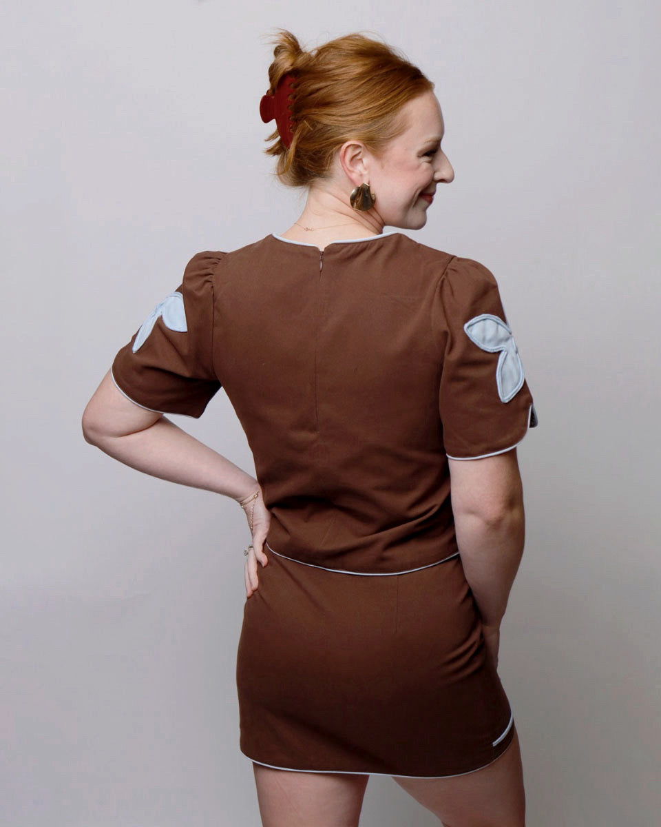 Woman wearing a brown dress with white patches on a plain background