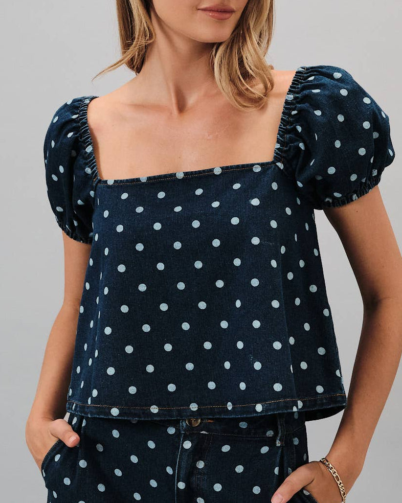 Woman wearing a navy blue top with white polka dots and matching pants on a gray background