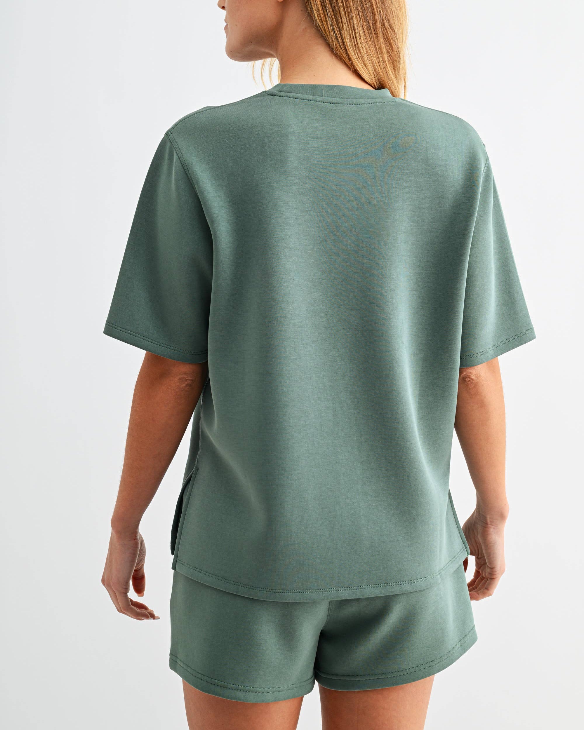Woman wearing a green t-shirt and shorts set on a white background back view
