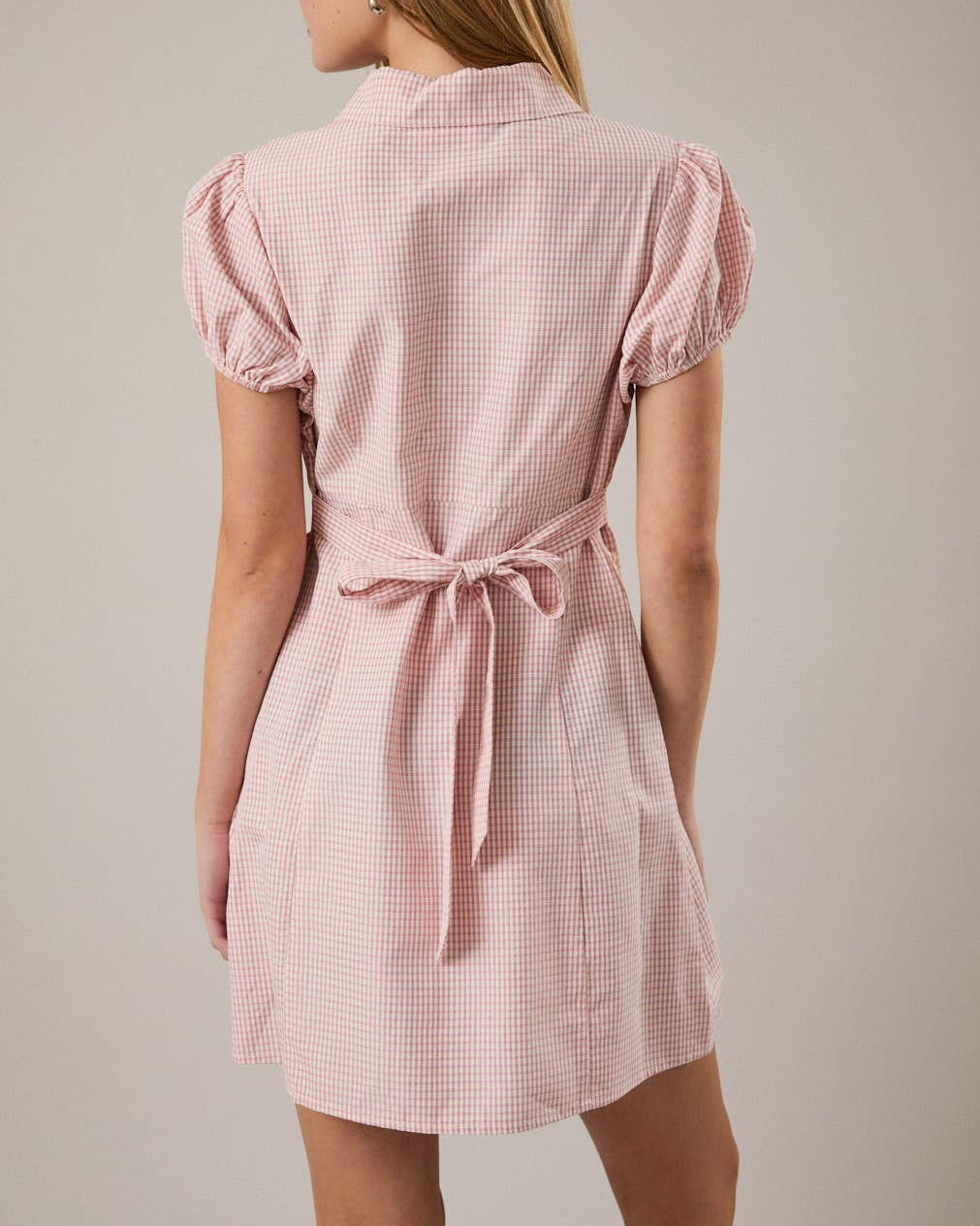 Woman wearing a pink checkered dress against a plain background