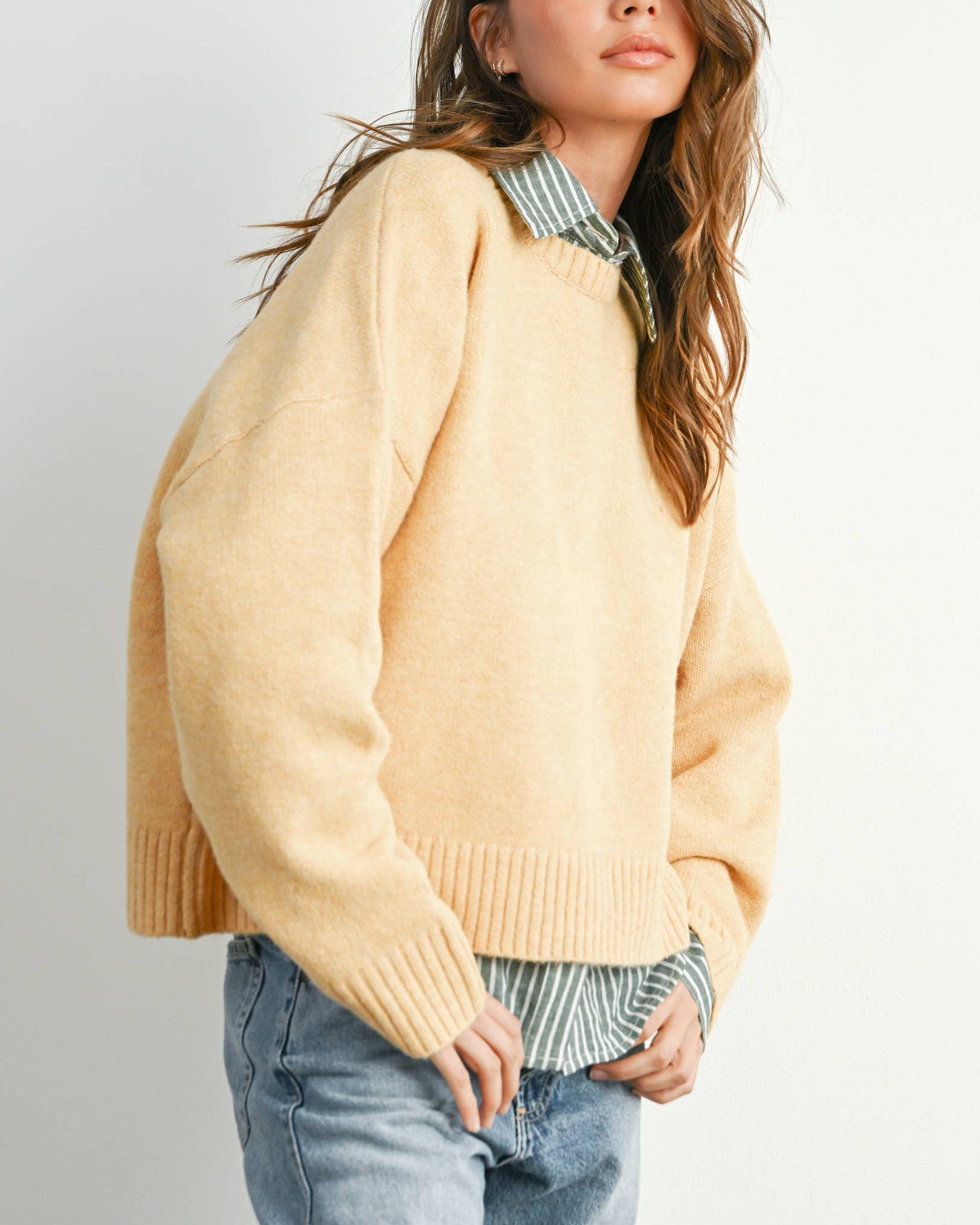 Woman wearing a yellow sweater and blue jeans against a plain background