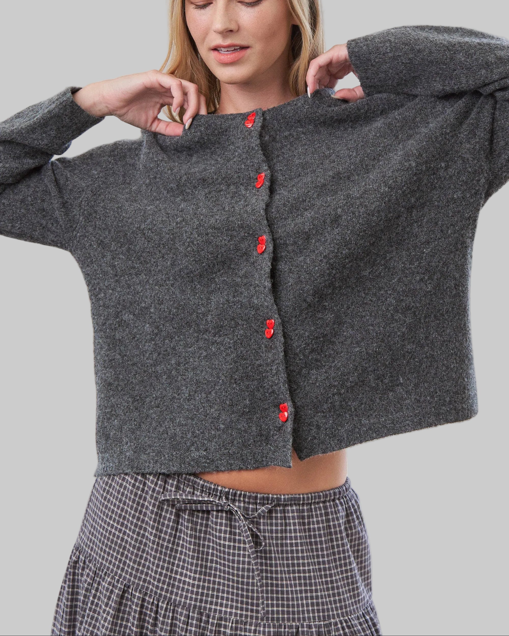 Woman wearing a gray cardigan with red buttons in a bright room.