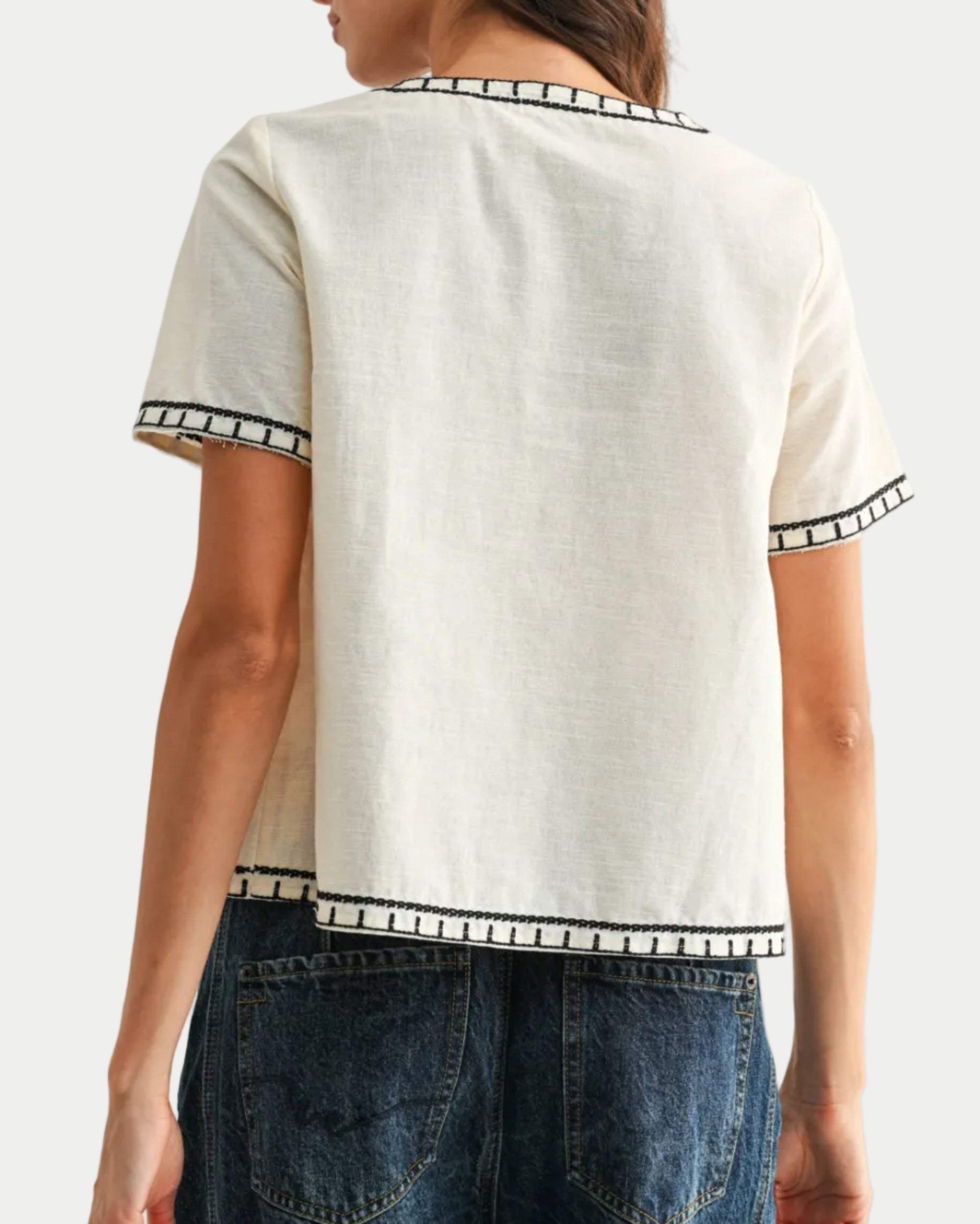 Woman wearing a white top with black trim and blue jeans on a plain background back view