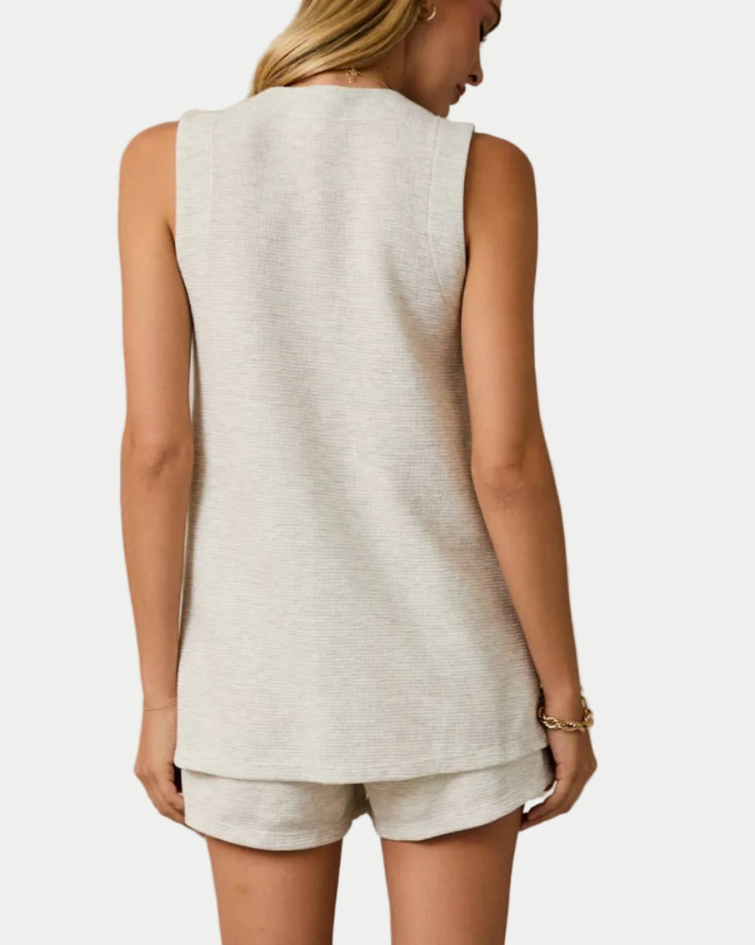 Woman wearing a sleeveless top and shorts with cowboy boots on a plain background