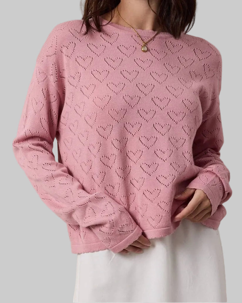 Woman wearing a pink sweater with heart patterns against a beige background