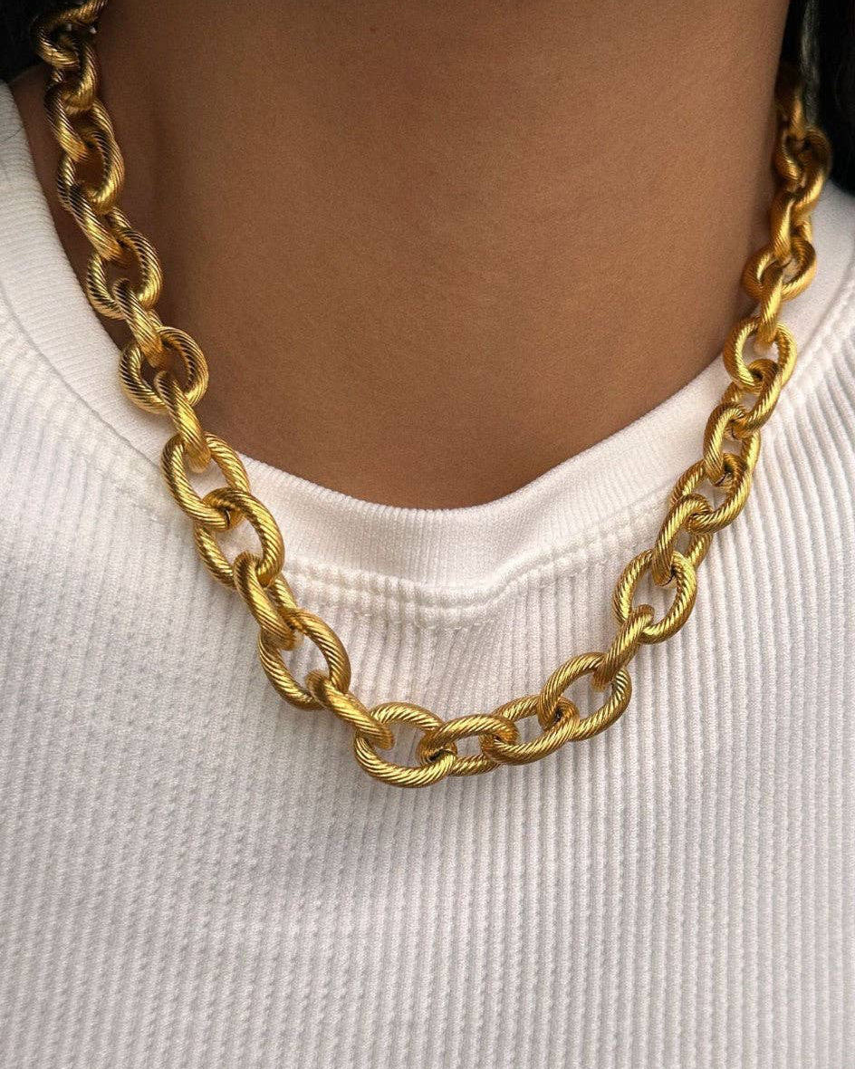 Gold chain necklace worn by a person on a white background