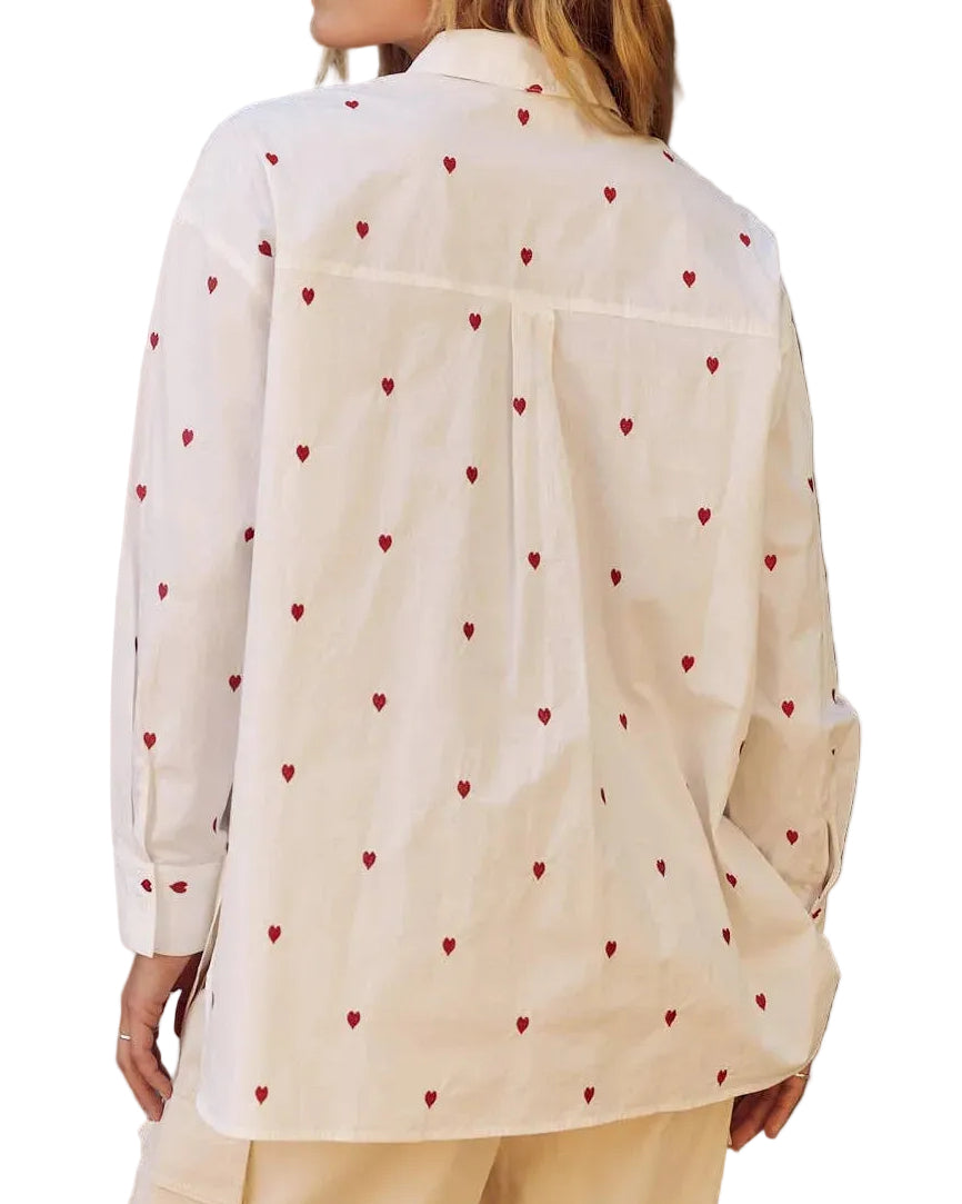 Person wearing a cream-colored blouse with red heart patterns outdoors.