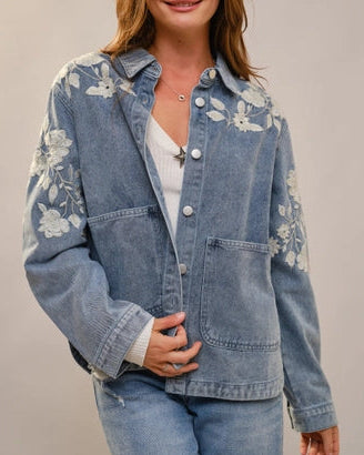 Woman wearing a floral embroidered denim jacket on a plain background