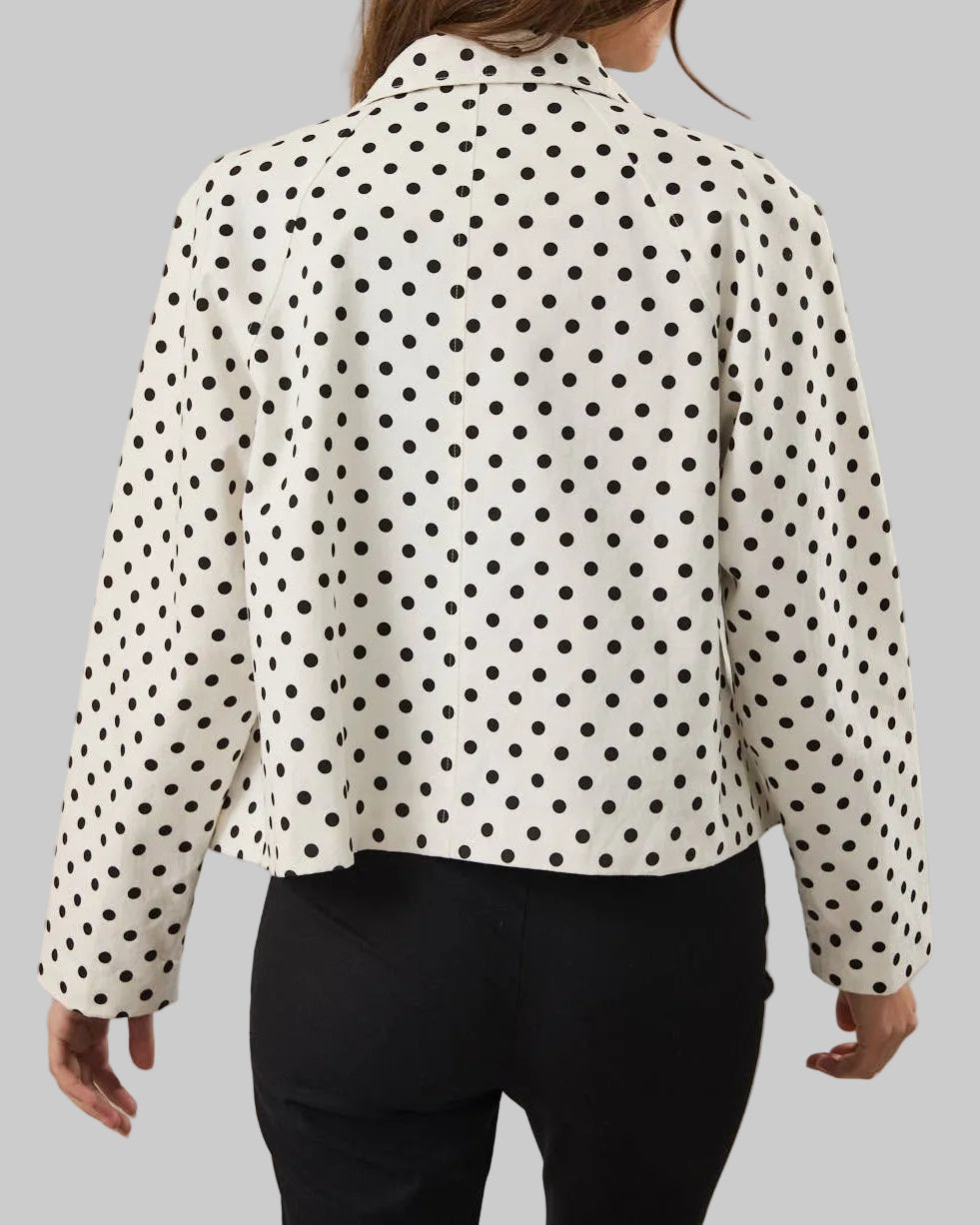 Person wearing a white blouse with black polka dots on a plain background