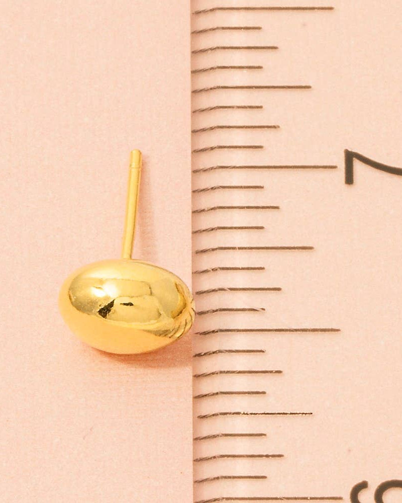 Gold earring next to a ruler on a pink background