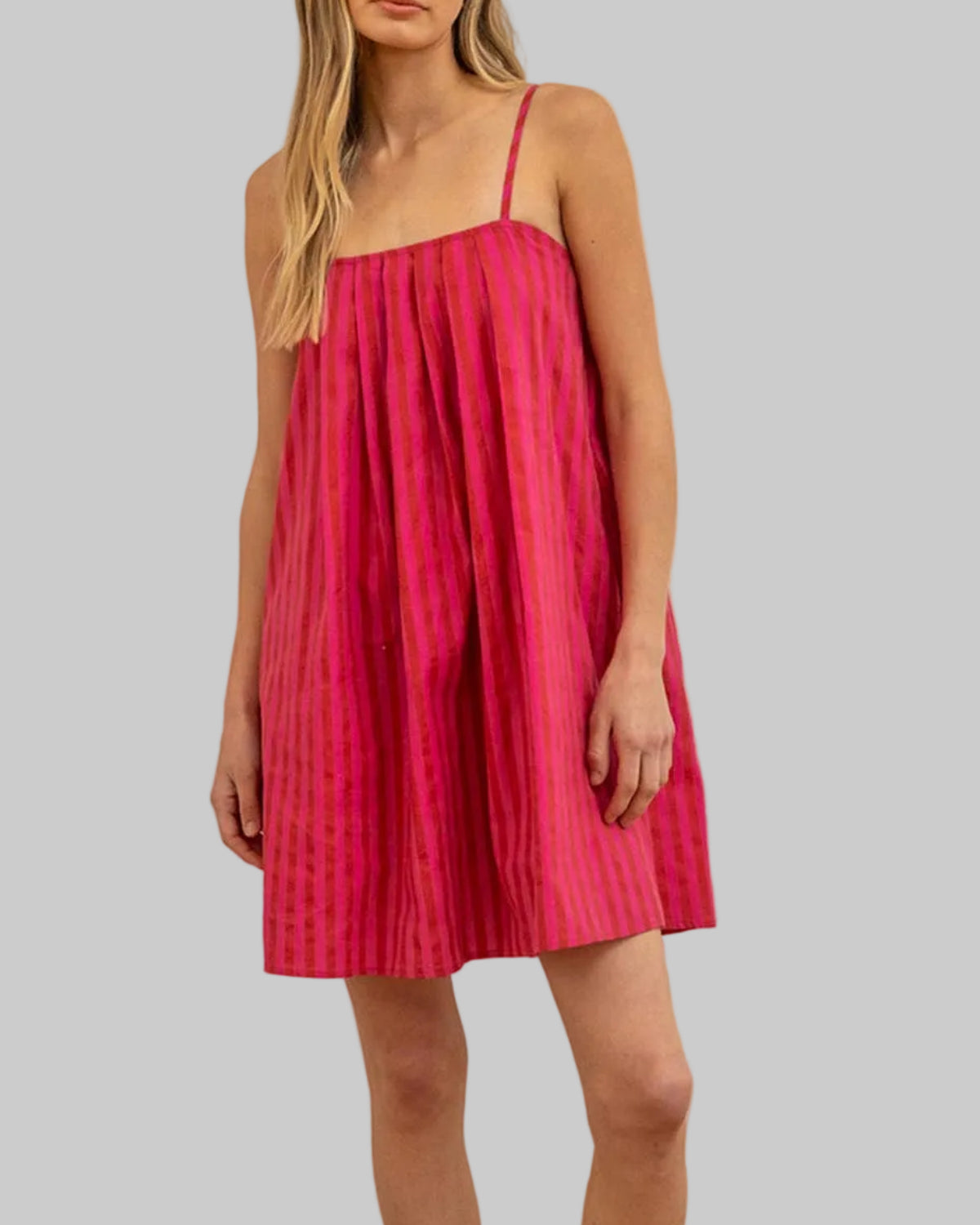 Woman wearing a pink dress standing in a room with wooden floor and white walls.