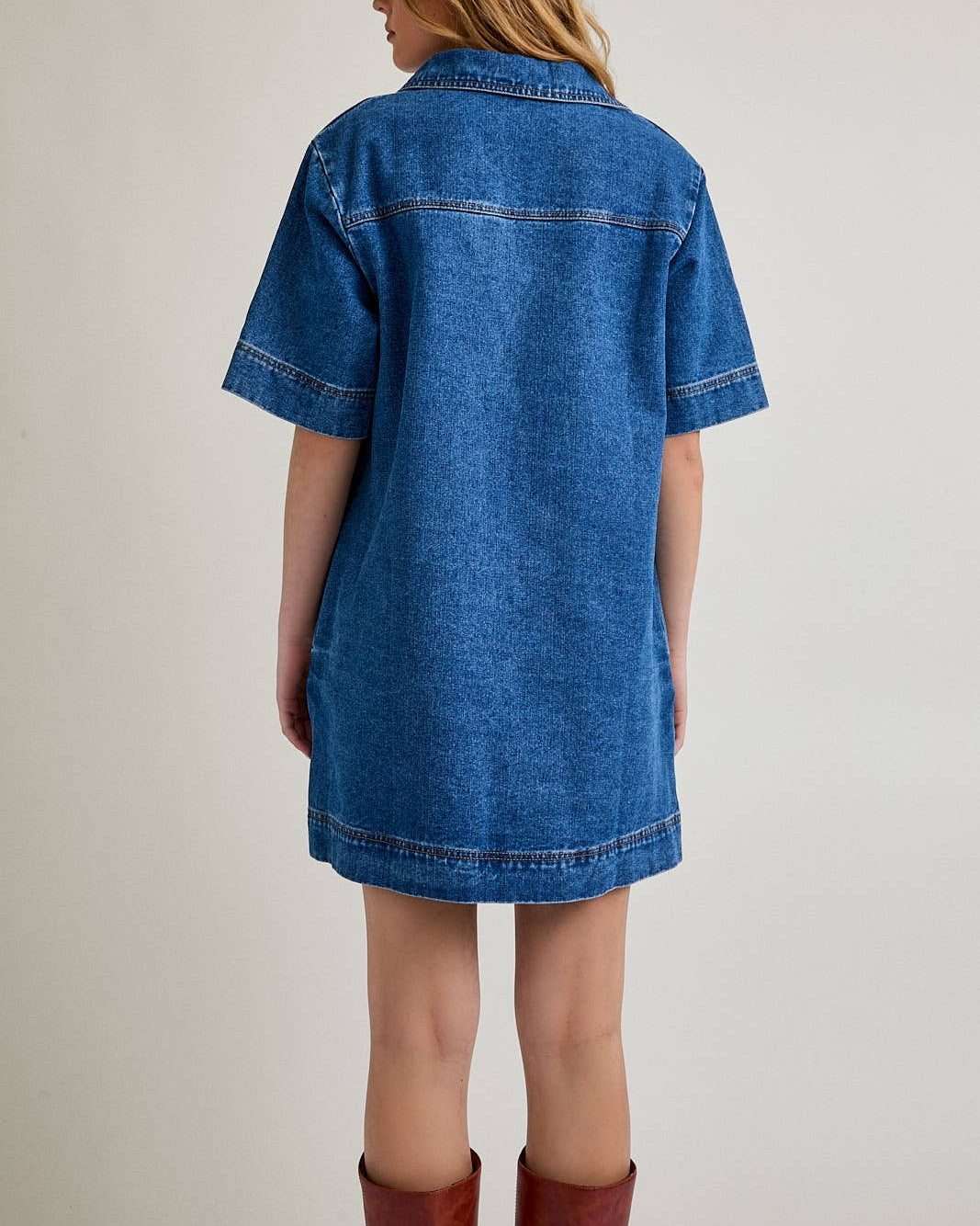 Person wearing a blue denim dress and brown boots on a plain background