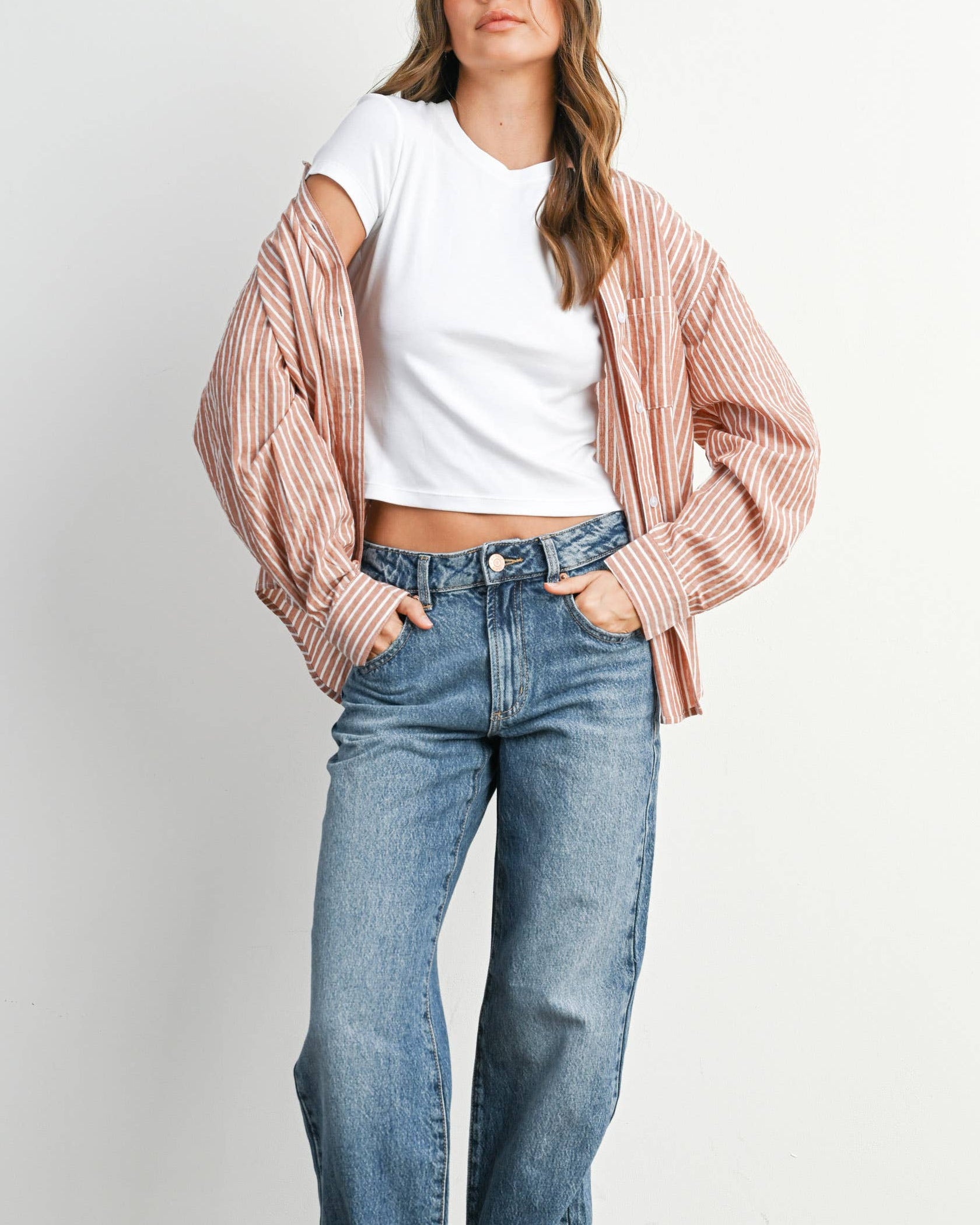 Woman wearing a white shirt, pink striped jacket, and blue jeans against a plain background