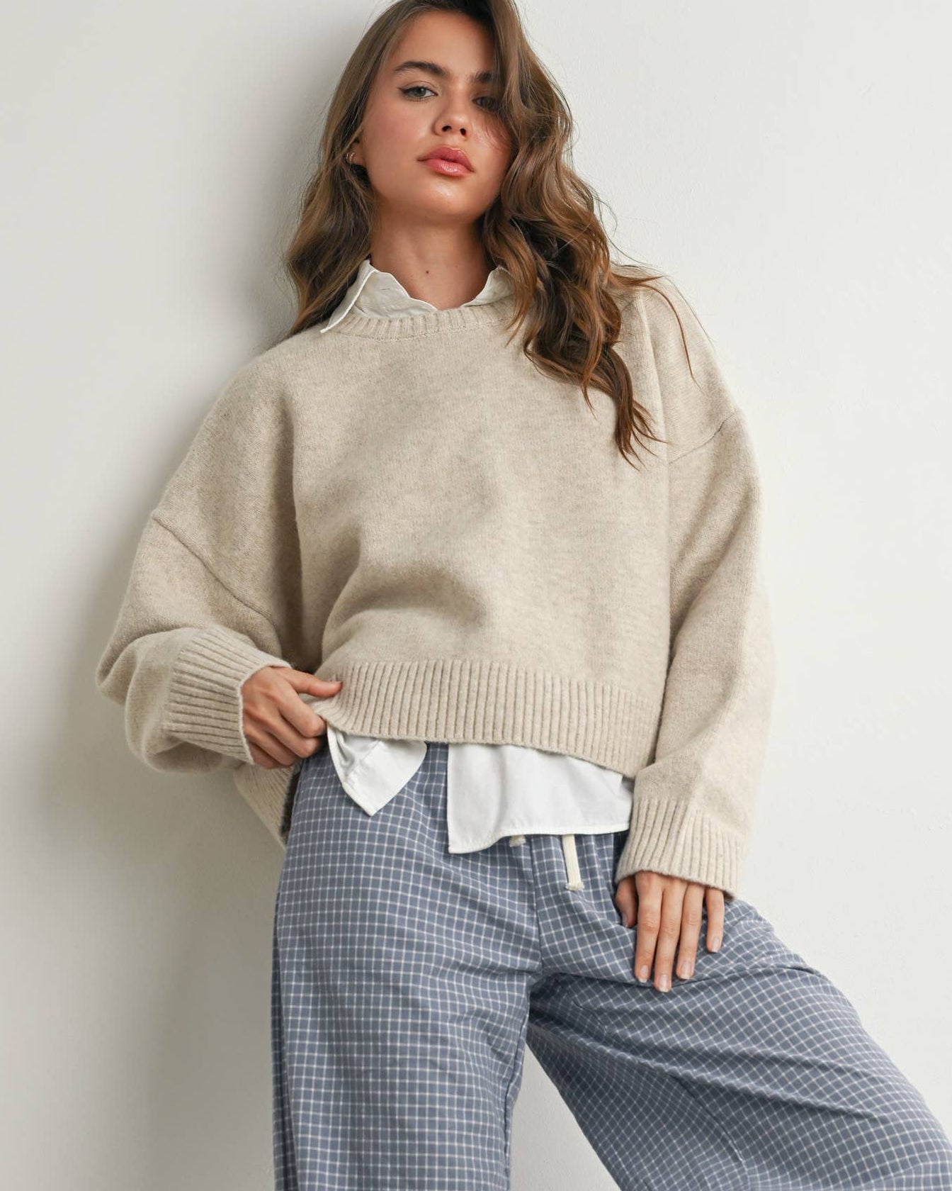 Woman wearing a beige sweater and blue checkered pants against a plain background