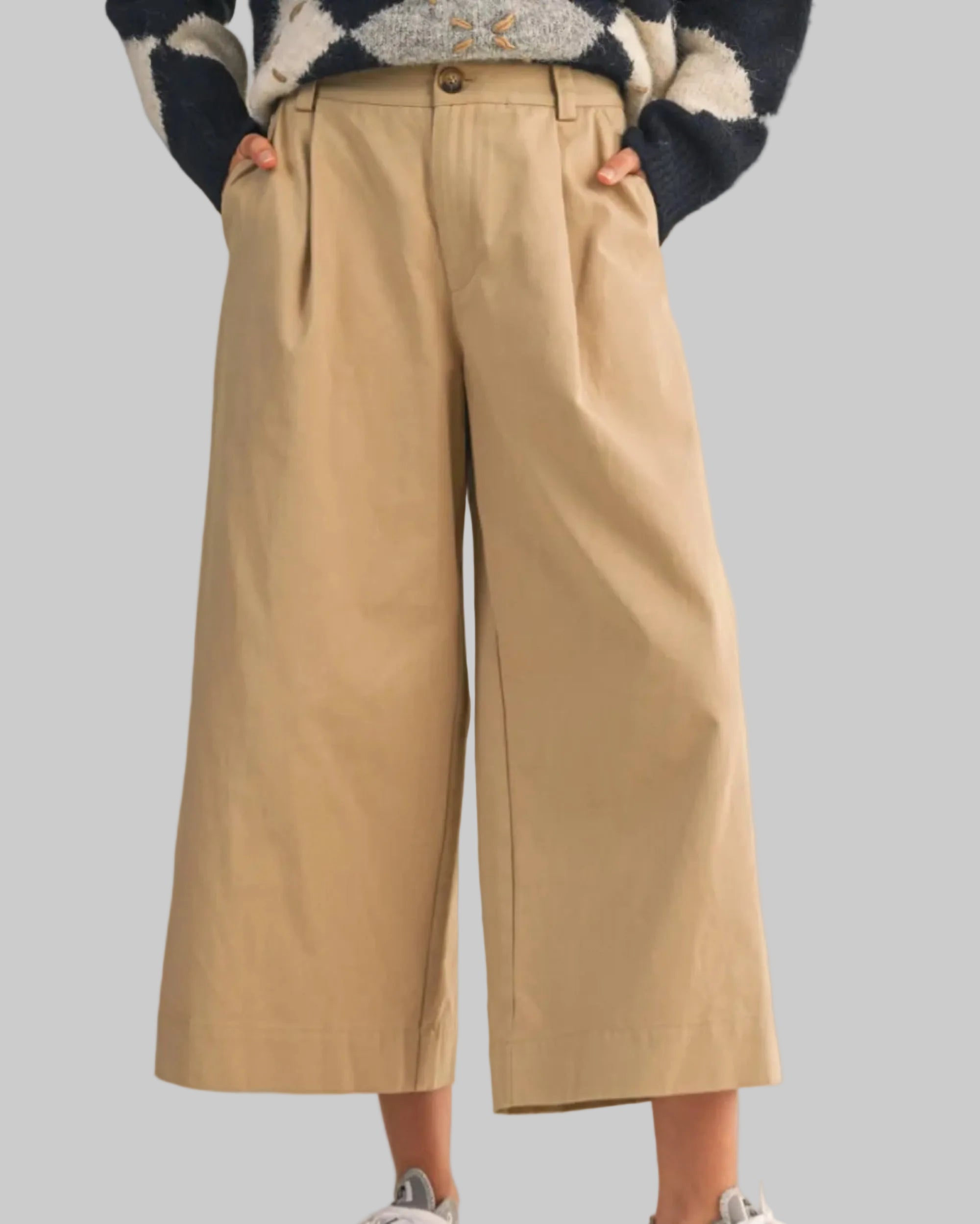 Person wearing beige wide-leg pants and gray sneakers on a beige background