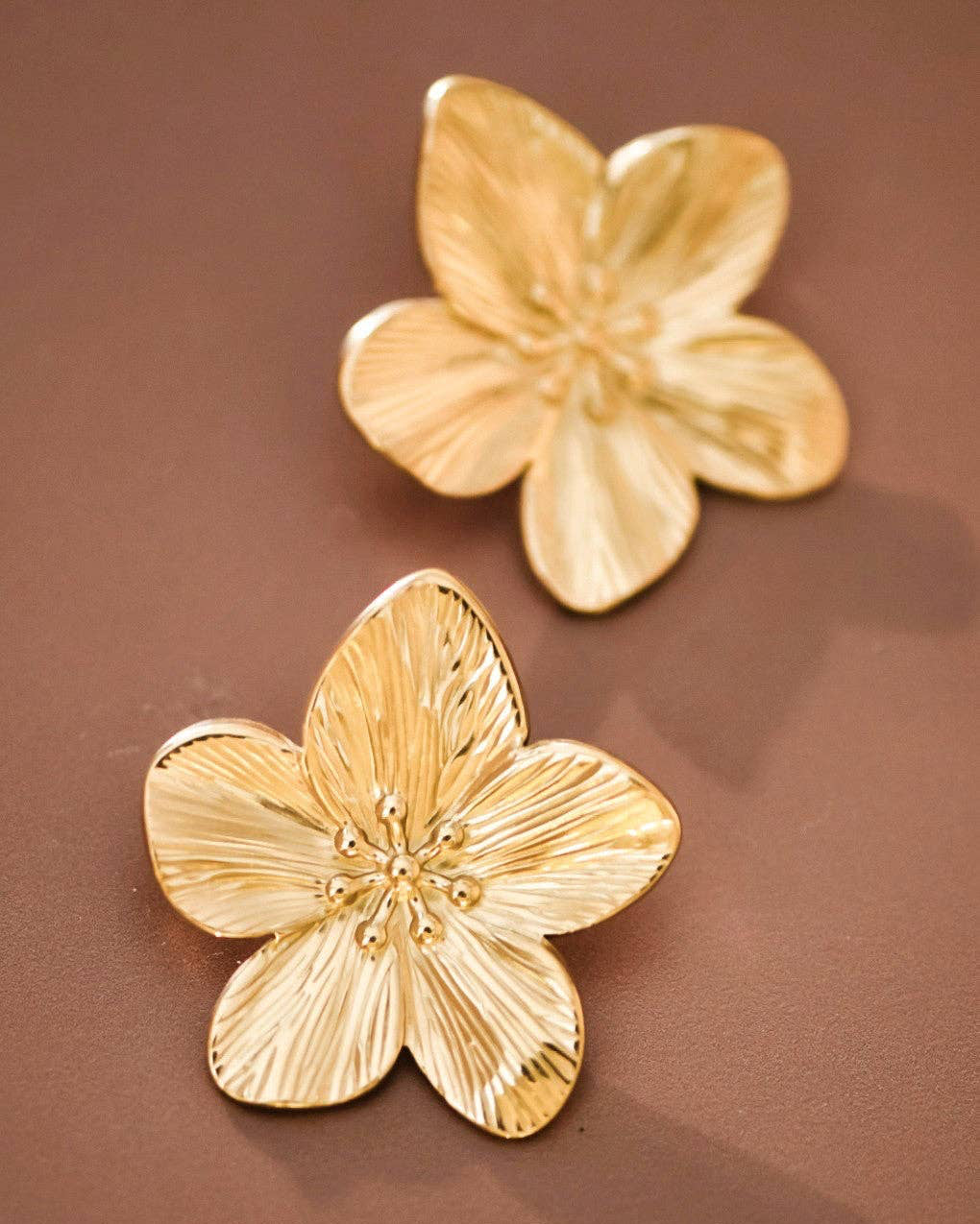 Pair of gold flower-shaped earrings on a brown background