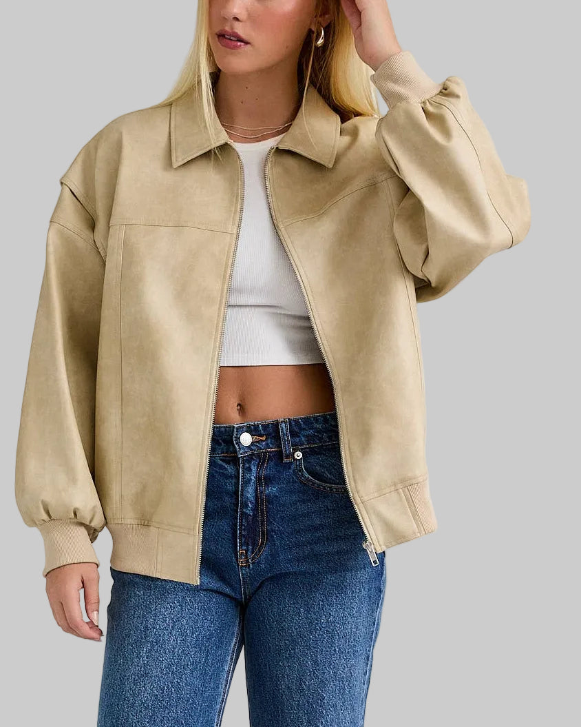 Woman wearing a beige jacket, white top, and blue jeans on a plain background