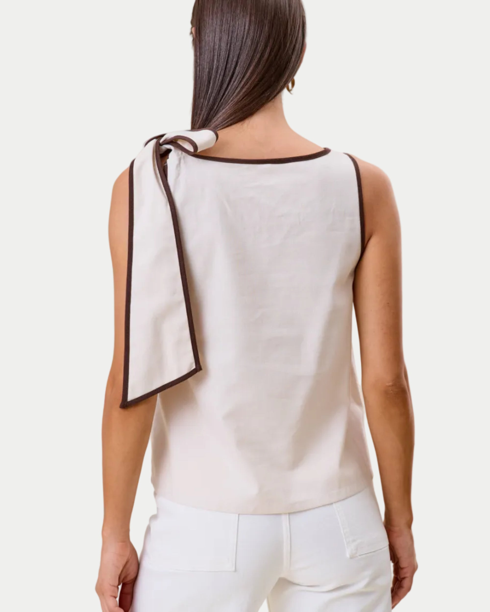 Woman wearing a beige sleeveless top with a black trim, standing against a beige background.