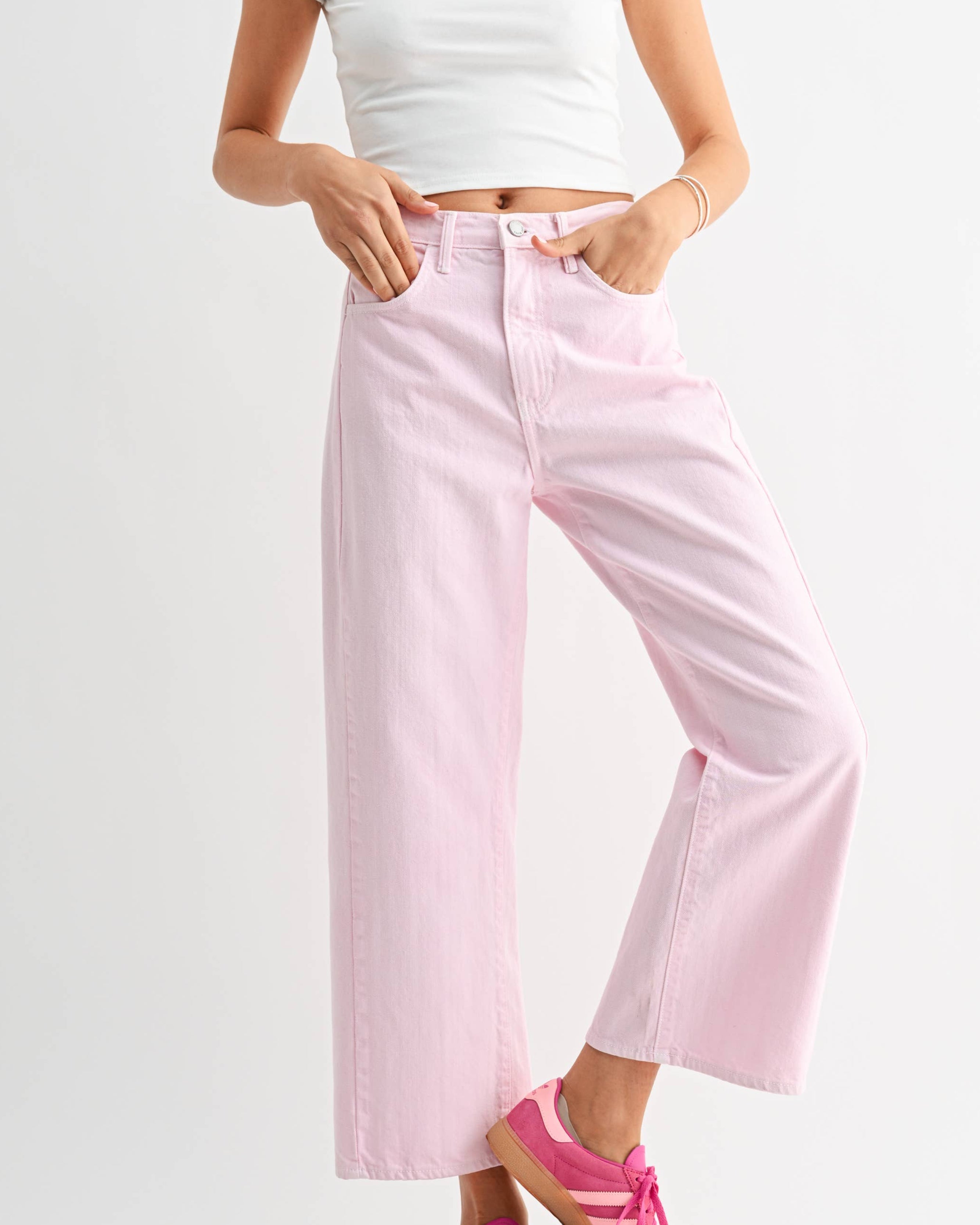 Woman wearing a white crop top with red designs and pink wide-leg jeans on a white background