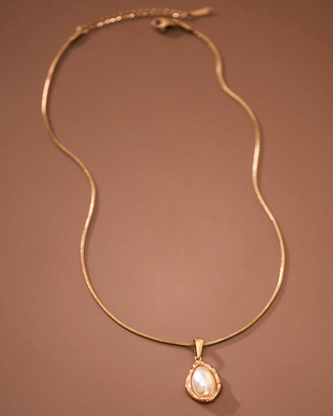 Gold necklace with a teardrop-shaped pearl pendant on a brown background