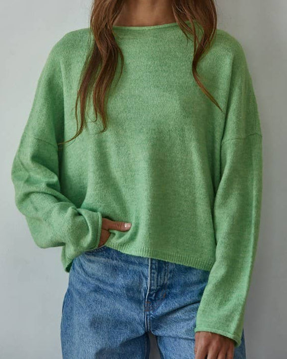 Woman wearing a green sweater and blue jeans against a plain background