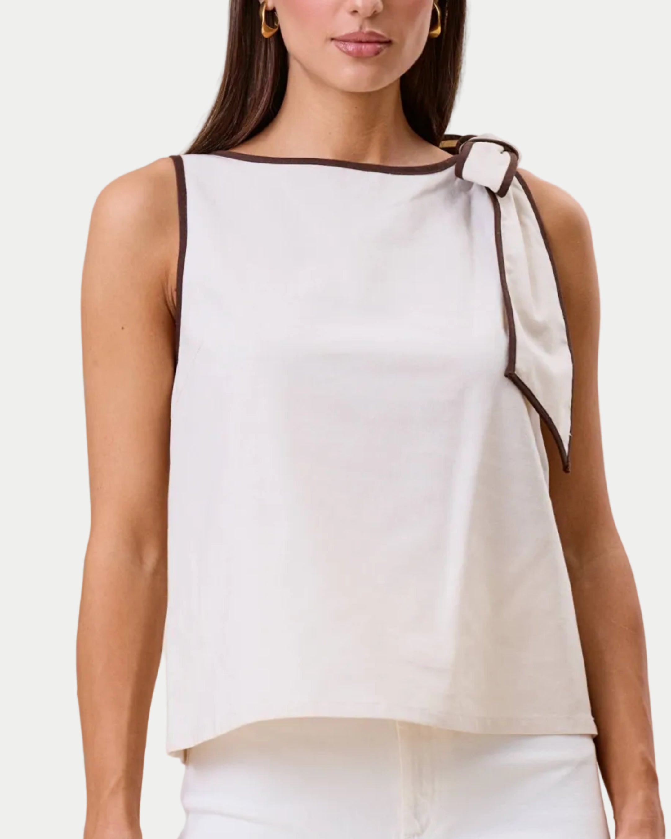 Woman wearing a white sleeveless top with a bow detail on a beige background