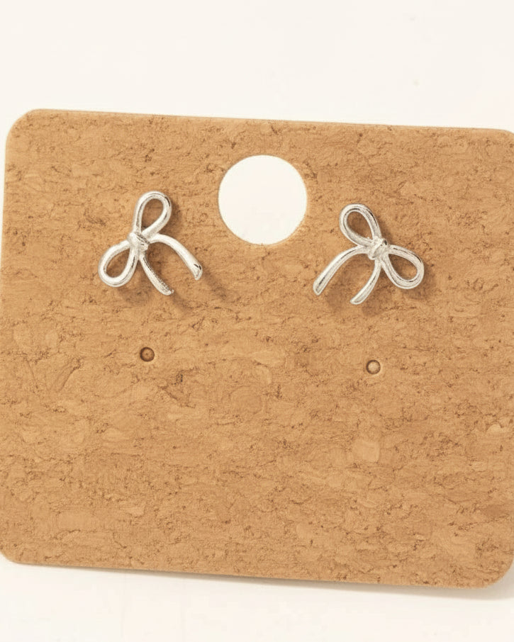 Pair of rhodium-plated bow-shaped earrings on a cardboard card with 'M' logo.