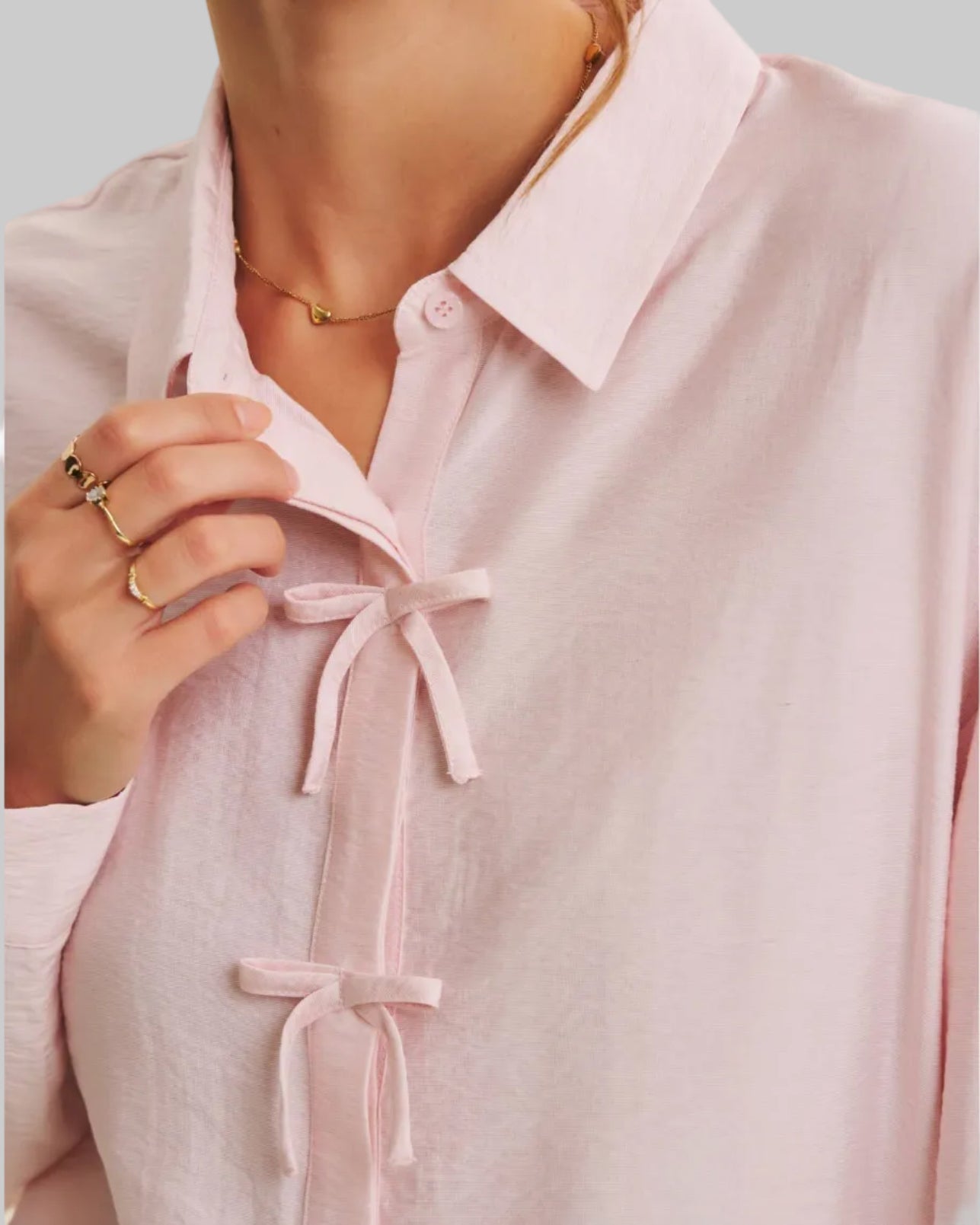 Pink blouse with tie details worn by a person, on a plain background