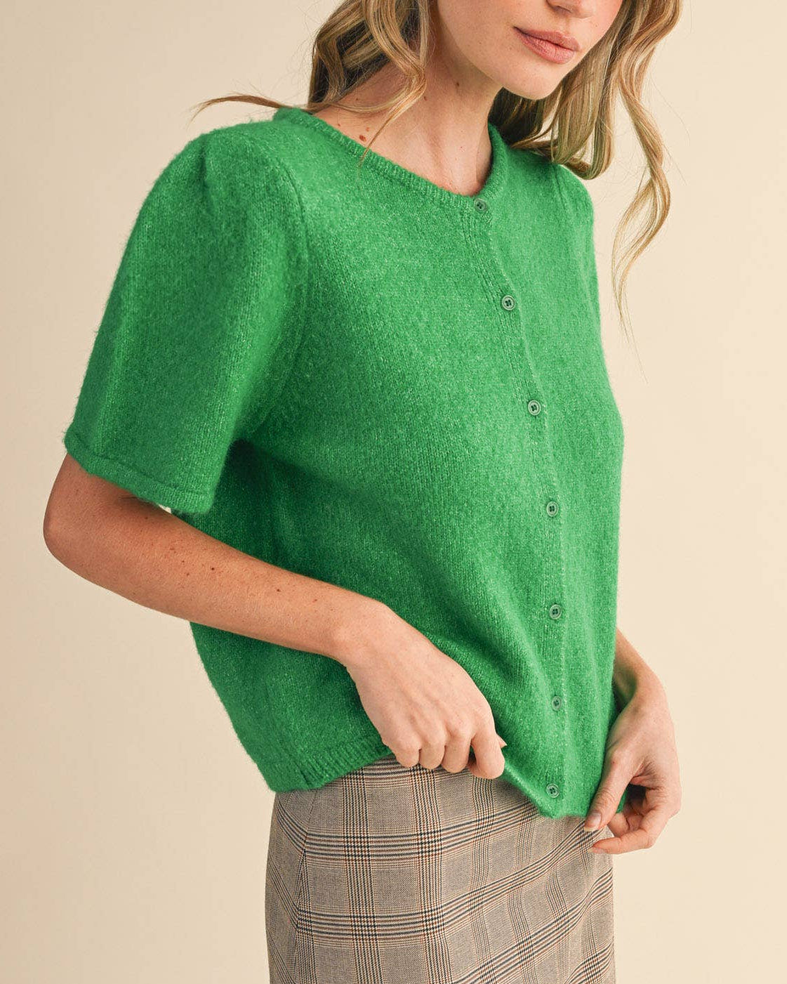 Woman wearing a green cardigan over a plaid skirt on a beige background