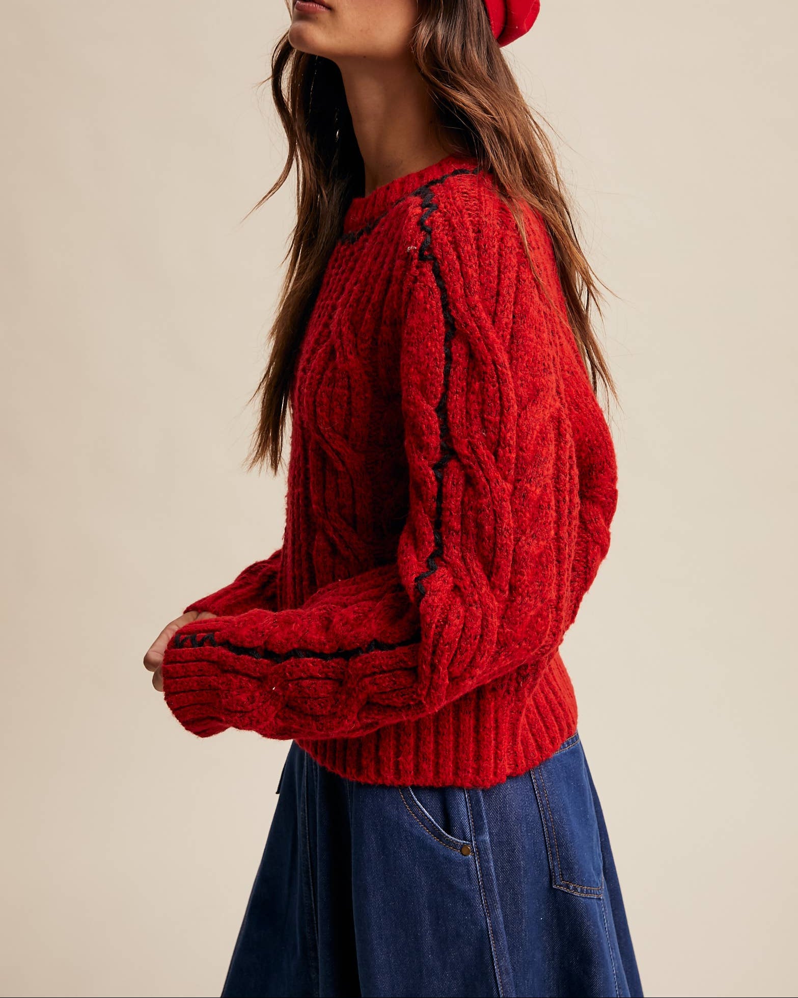 Woman wearing a red knitted sweater and matching red cap against a beige background