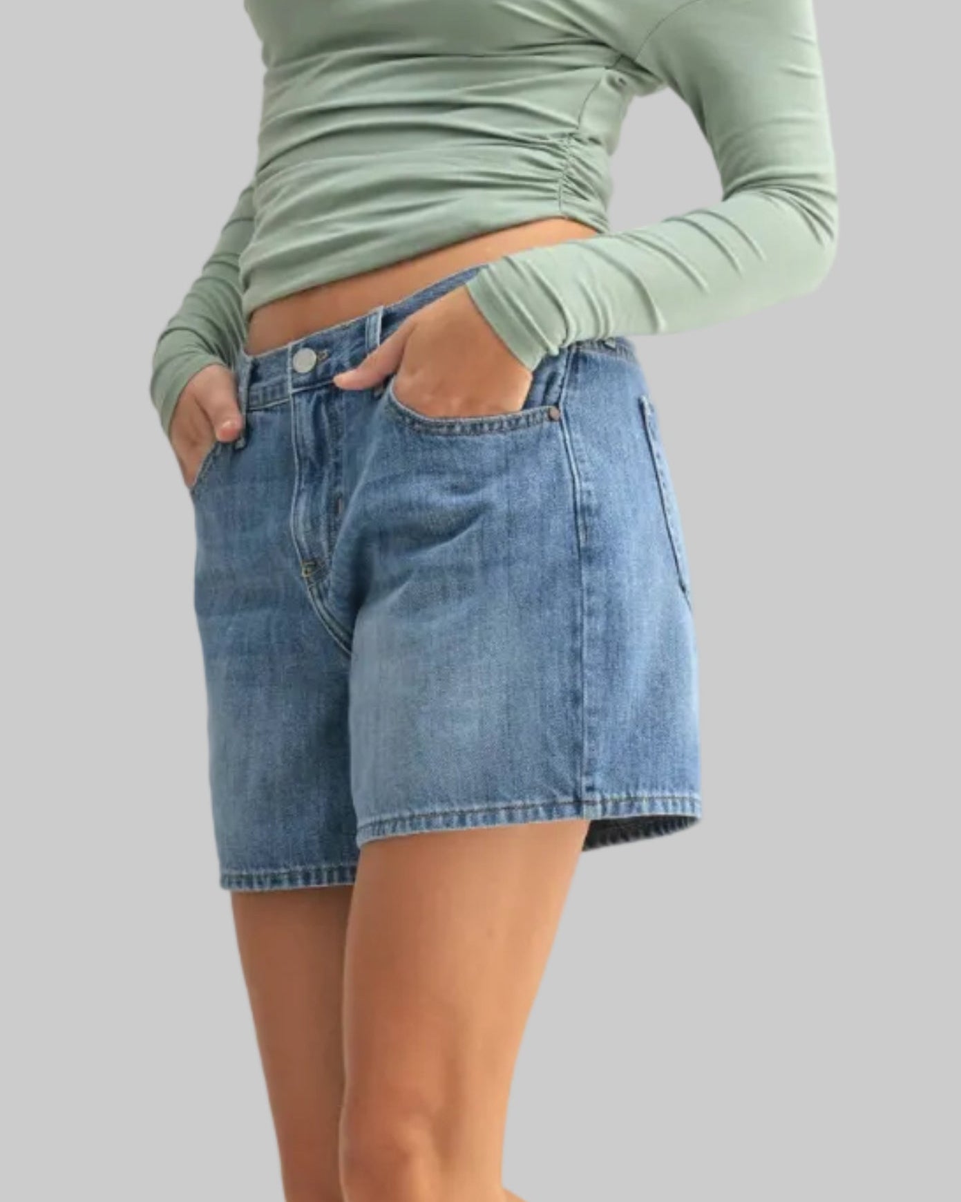 Woman wearing a green off-shoulder top and denim shorts on a white background