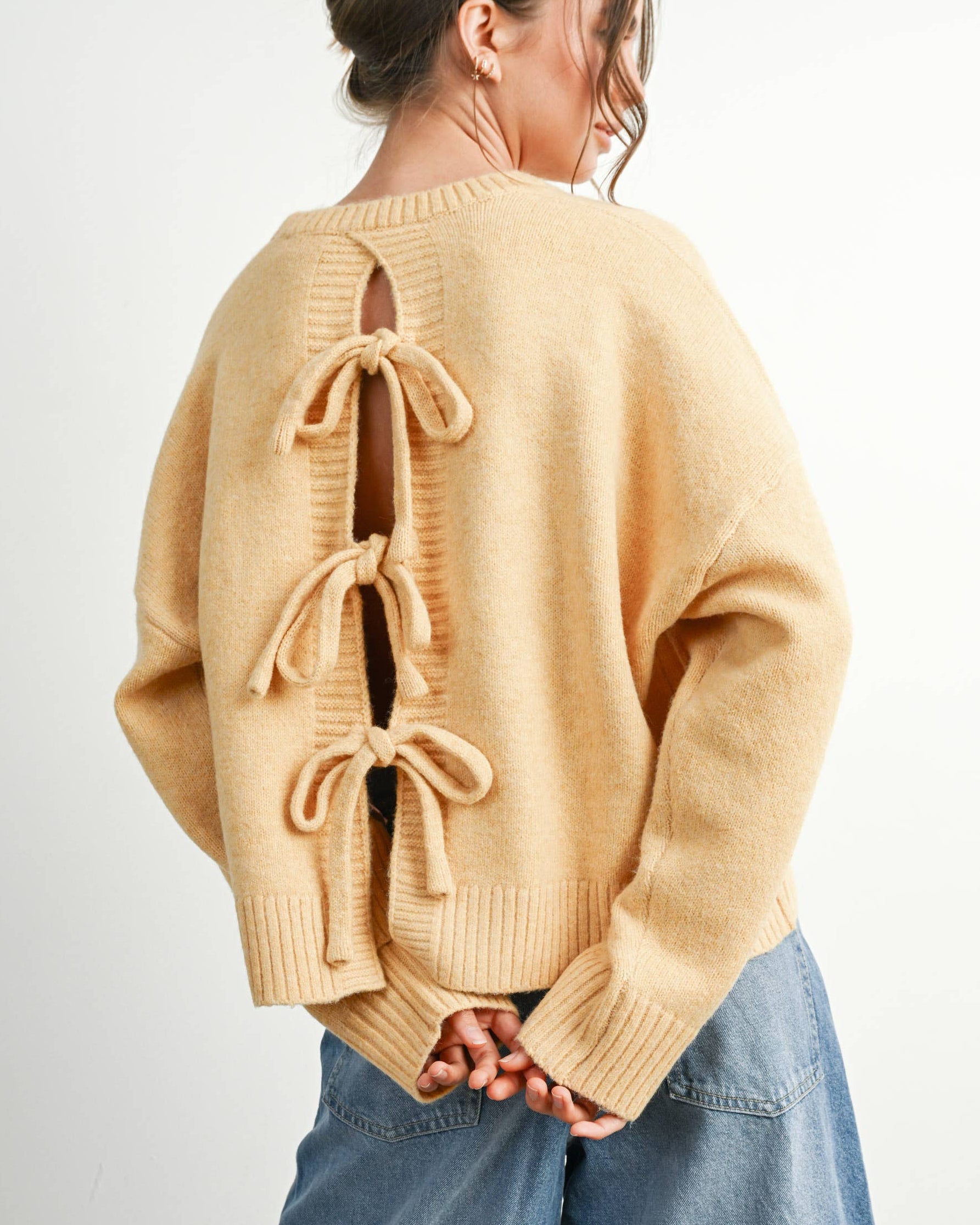 Person wearing a beige sweater with bow details on a plain background