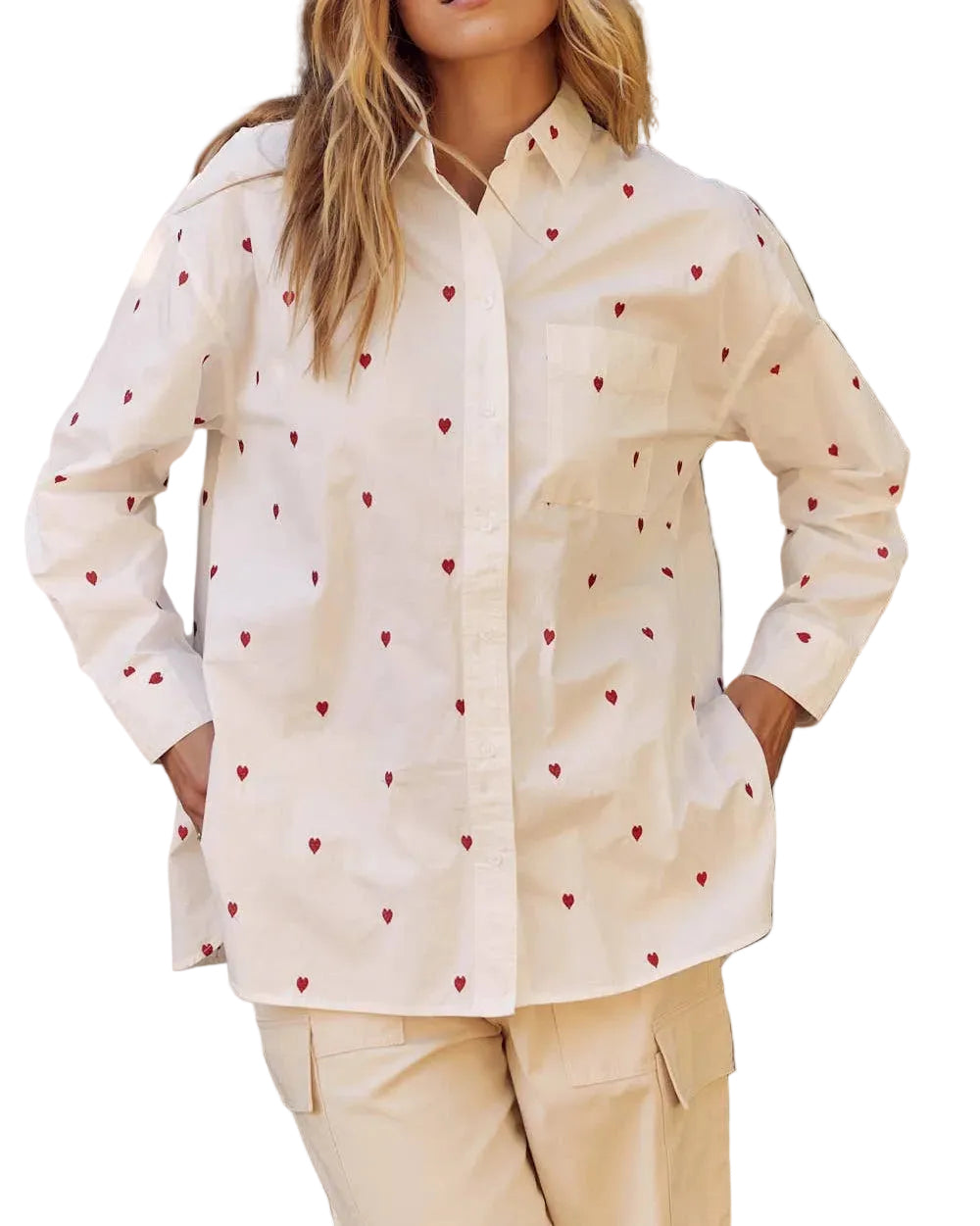 Woman wearing a cream-colored shirt with red heart patterns and beige pants outdoors.