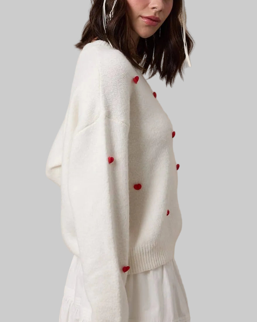 Woman wearing a white sweater with red heart patterns against a beige background