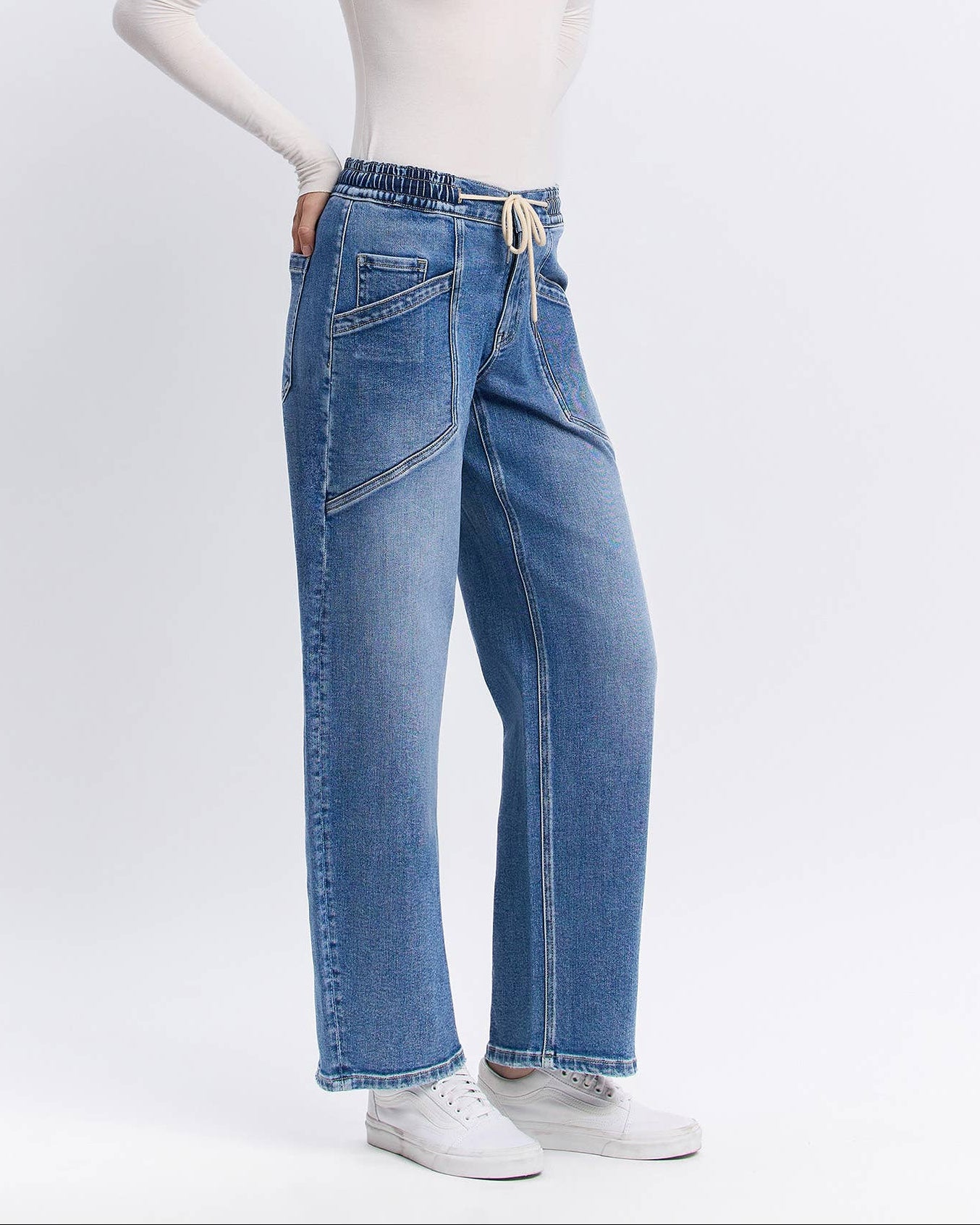 Woman wearing a white long-sleeve top and blue jeans on a white background