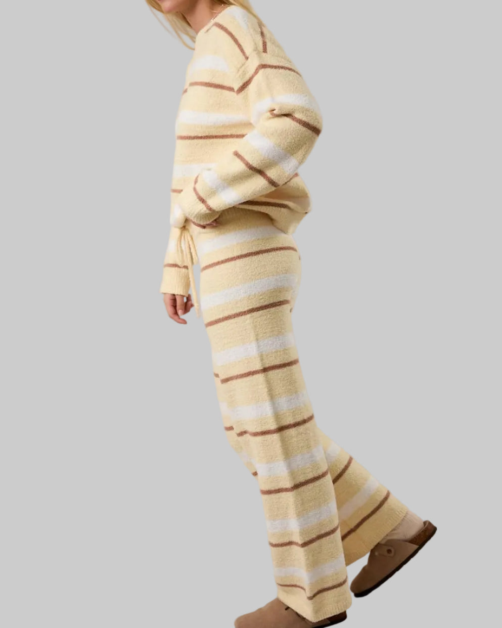 Woman wearing a yellow and white striped sweater and pants on a plain background