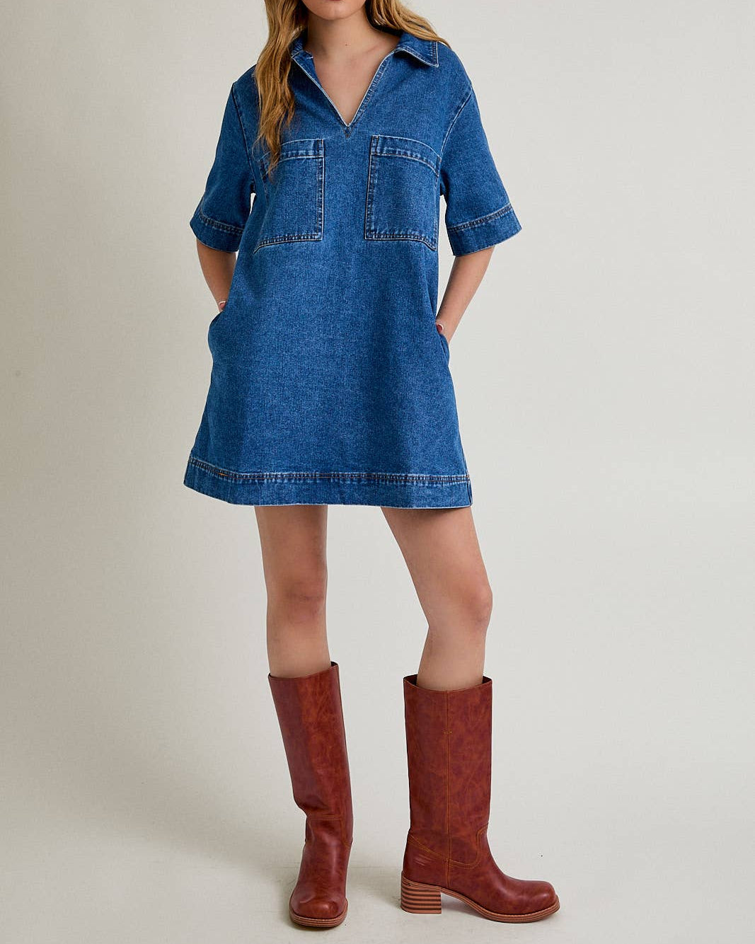 Woman wearing a blue denim dress and red boots on a beige background