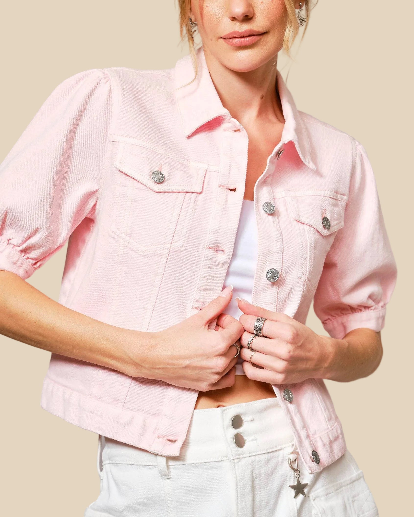 Woman wearing a light pink denim jacket over a white shirt and light blue jeans on a gray background