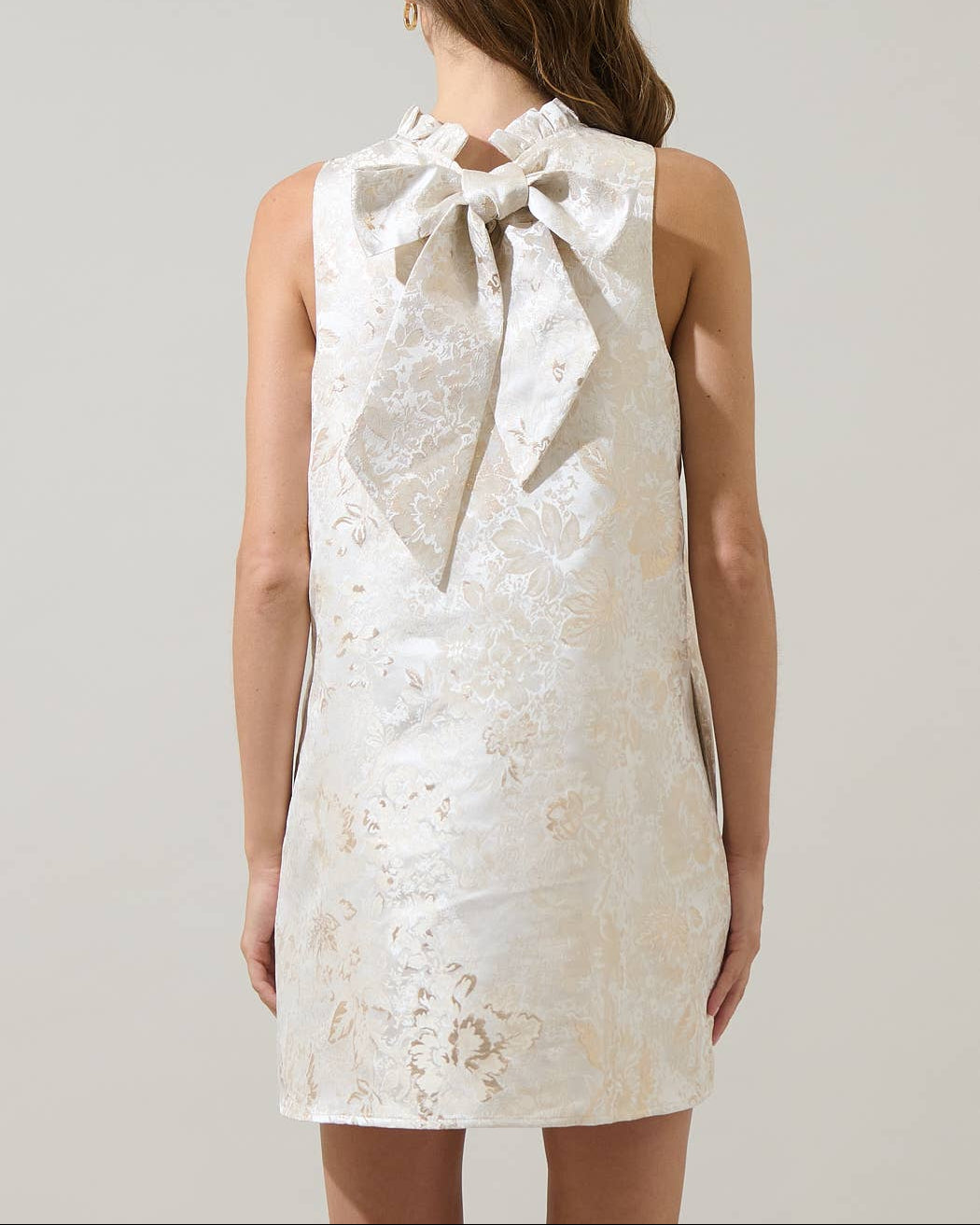 White jacquard dress with a large bow on the back worn by a person against a plain background